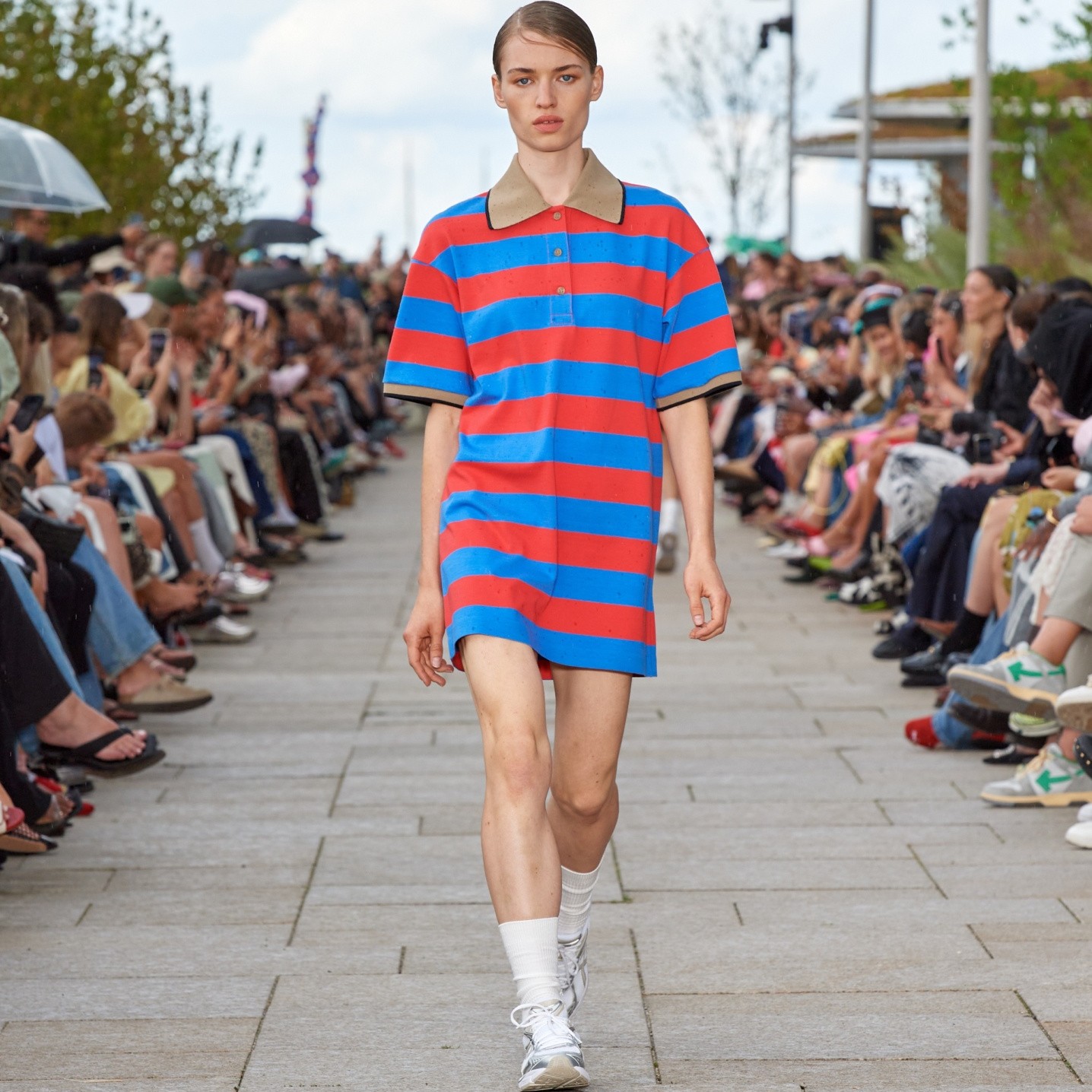 Model walking on the catwalk of the fashion show dressed in a blue-red Reference tunic.