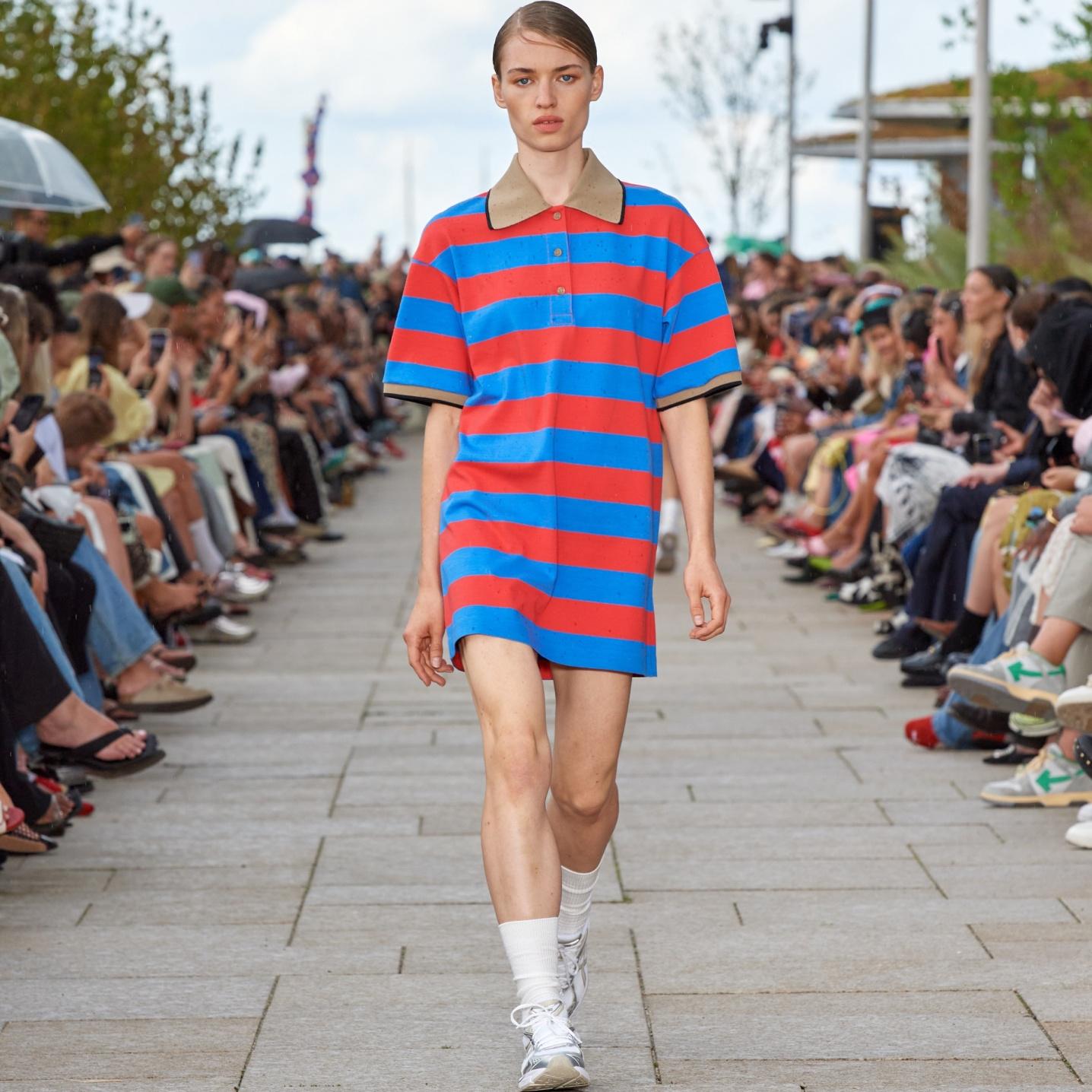 Model walking on the catwalk of the fashion show dressed in a blue-red Reference tunic.