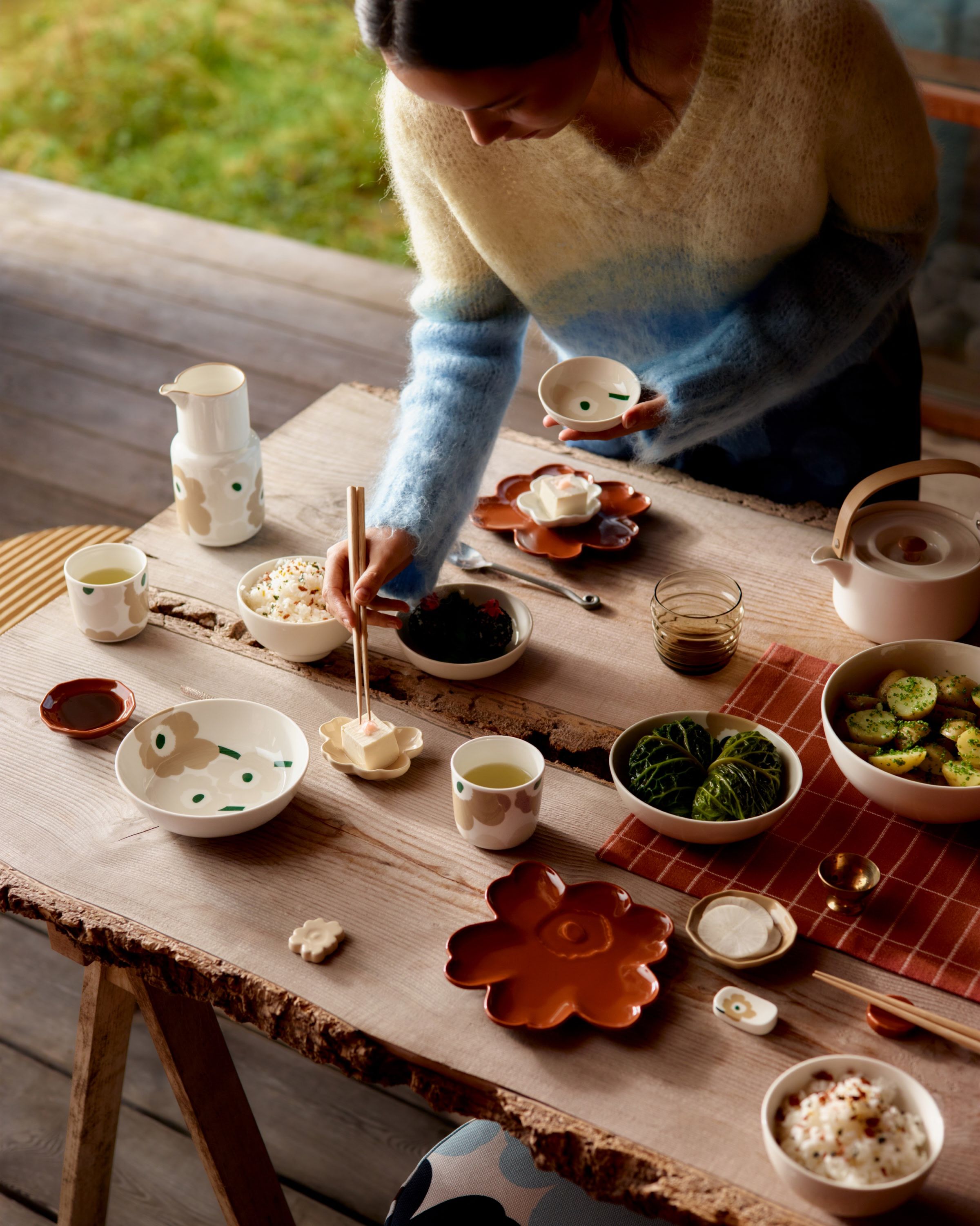 Model picking food with chopsticks from a table set with beige and red Unikko-print tableware.