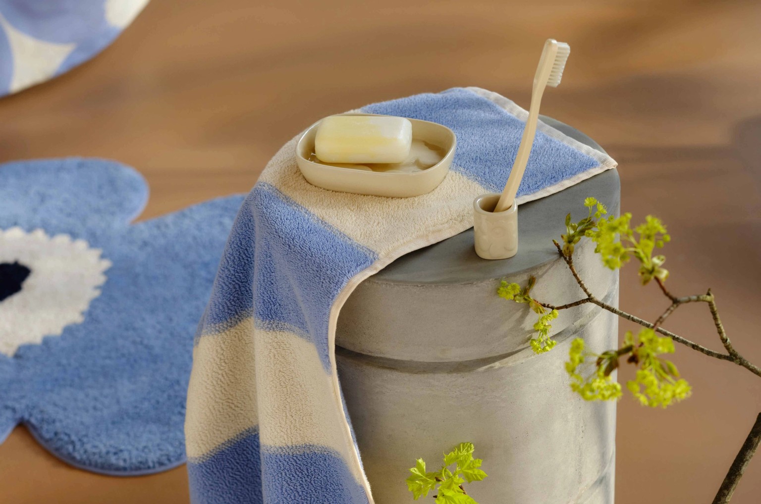 Blue and white striped towel, blue Unikko-shaped bath mat and a glass vase with a twig on the floor