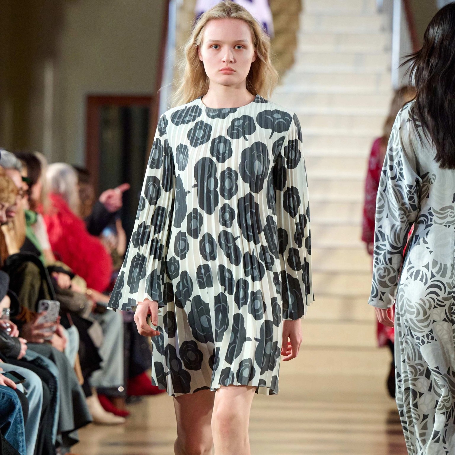 A model walks in the Marimekko fashion show wearing a gray and white pleated dress.