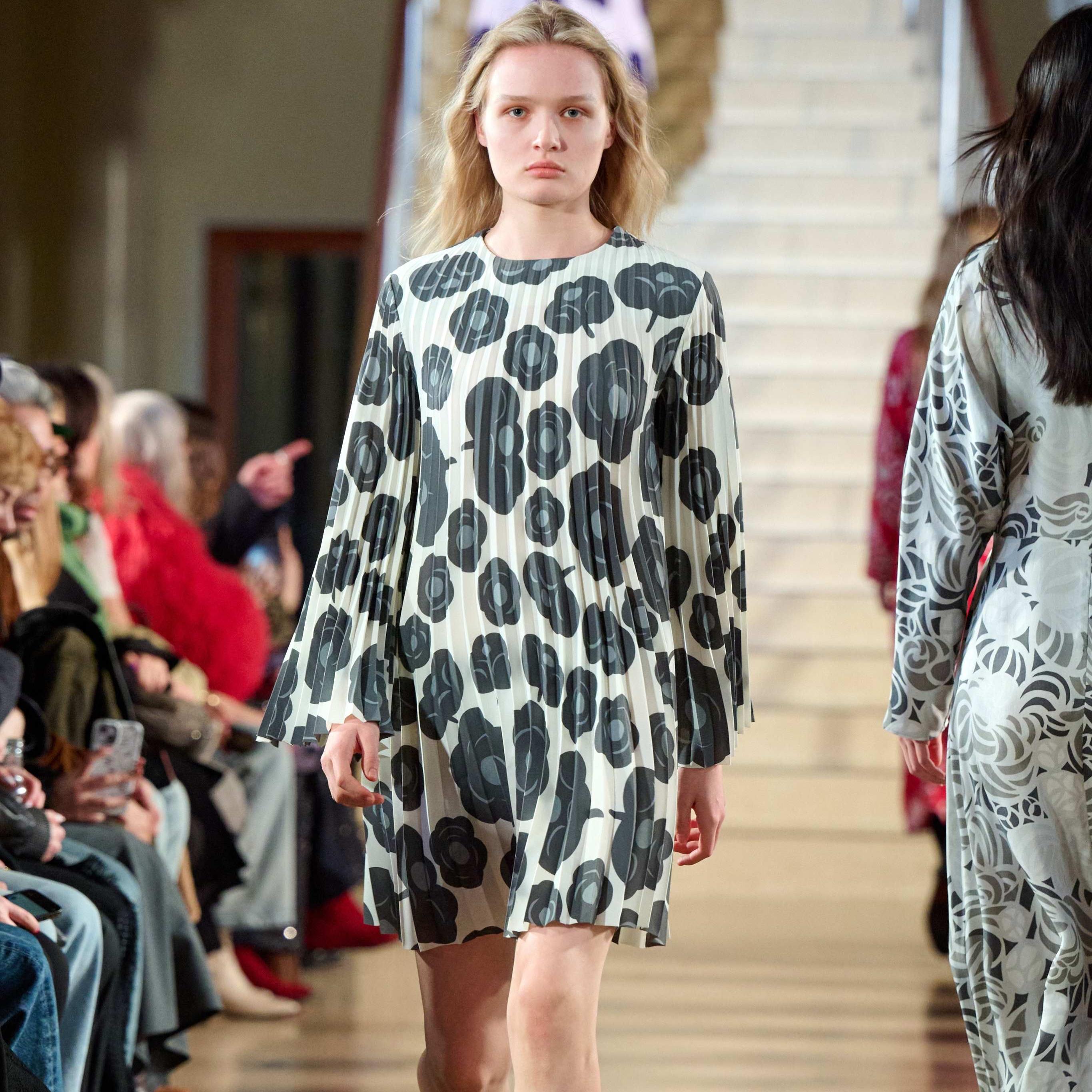 A model walks in the Marimekko fashion show wearing a gray and white pleated dress.