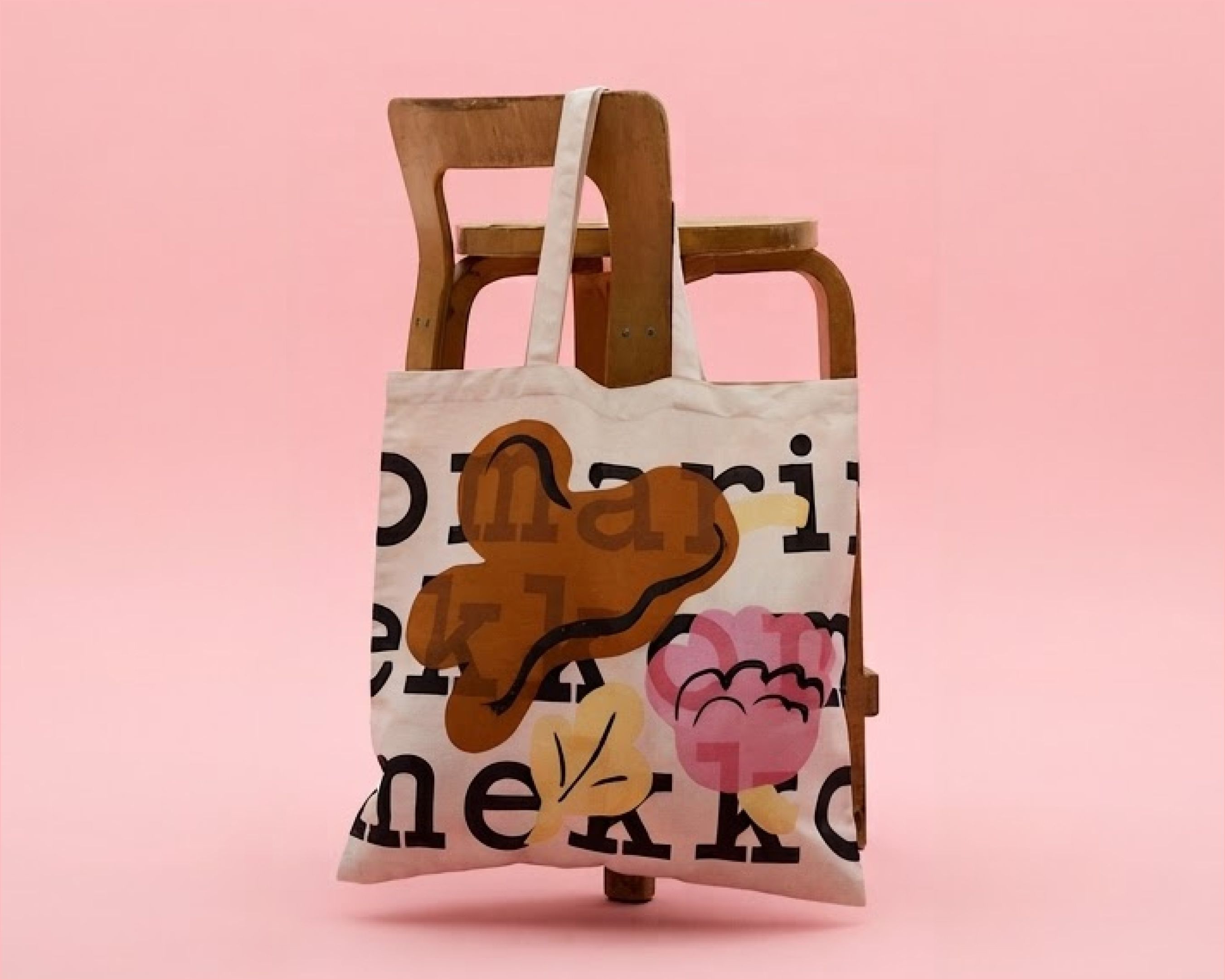 Logo tote, with a logo text and Kukasta kukkaan print in brown and yellow.