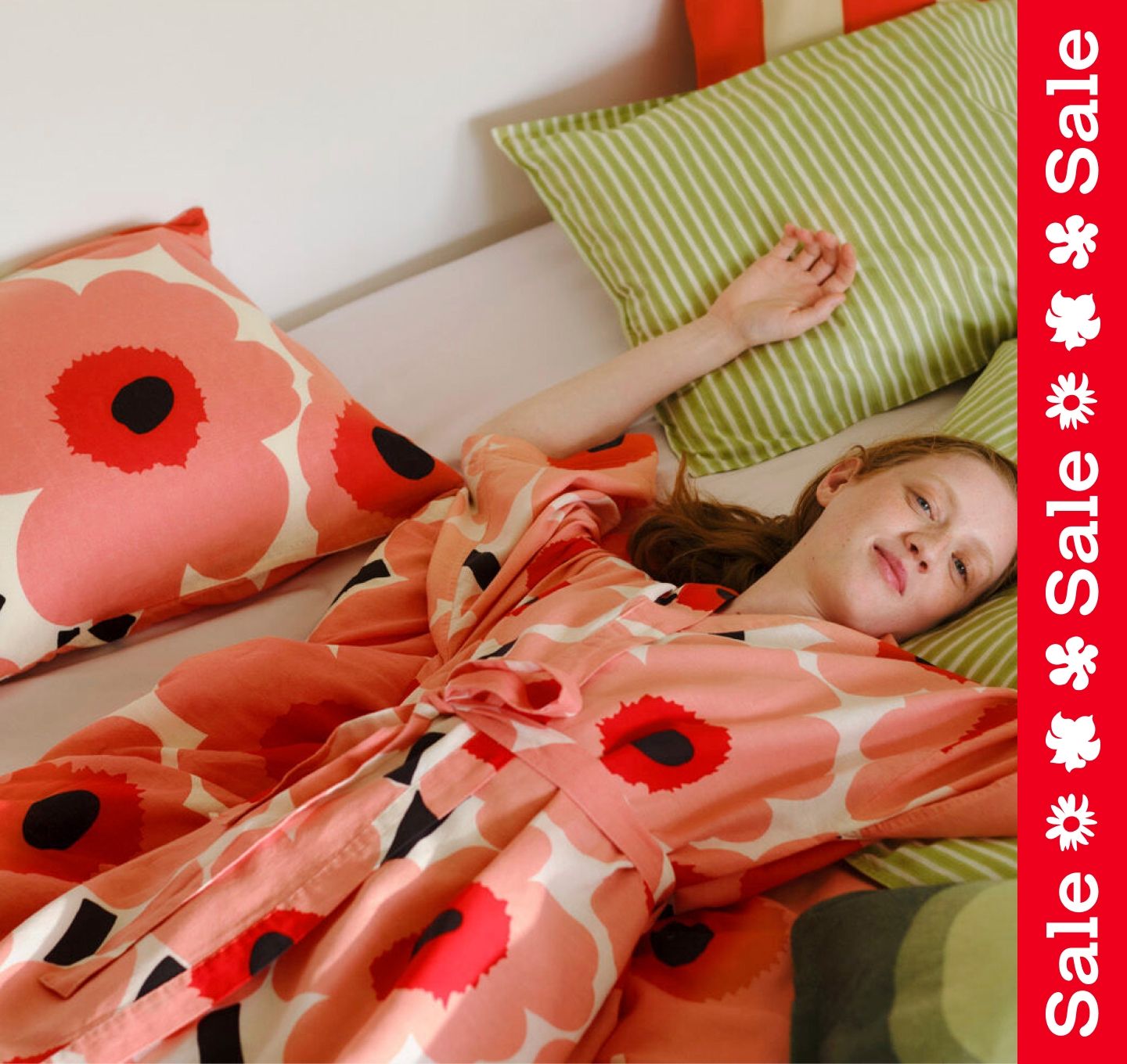 Model laying on bed with Unikko and Piccolo printed duvet covers and pillow cases in a Unikko printed robe. Right edge has a vertical Sale stripe.