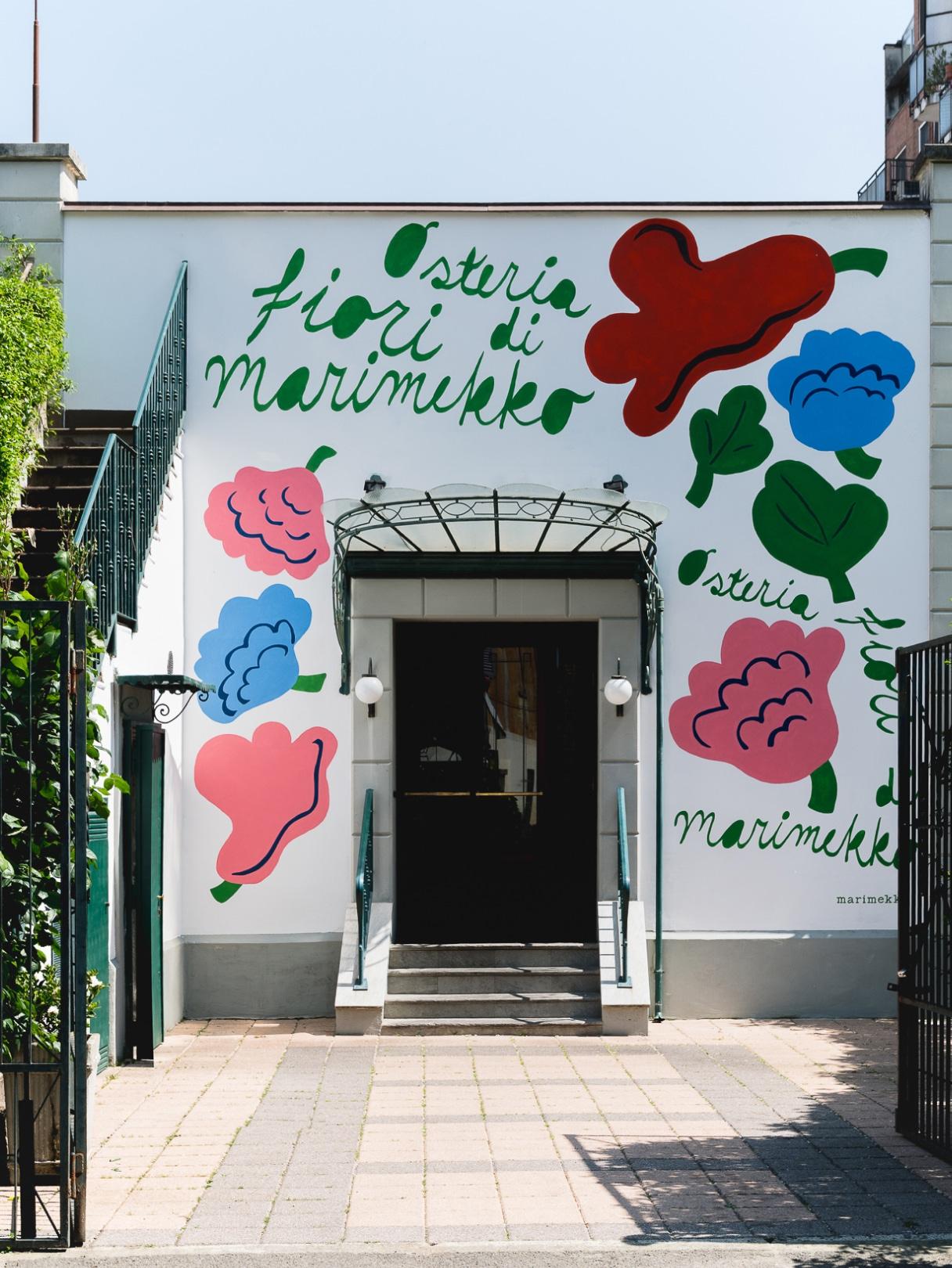 Exterior of a house featuring the Kukasta kukkaan pattern painted on it, along with the text “Osteria Fiori di Marimekko.”