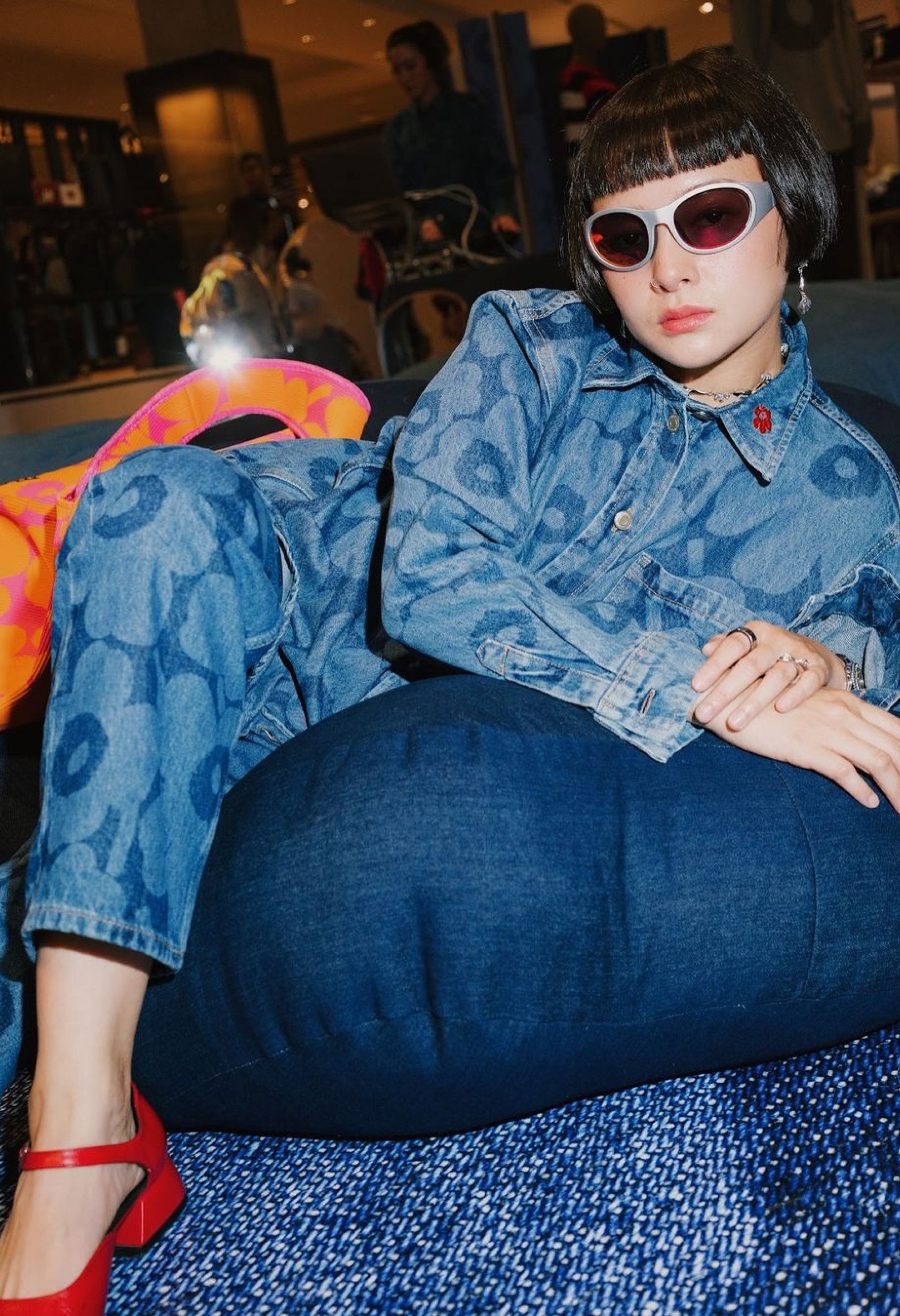 Supanaree leans against a pillow, dressed in a Unikko denim outfit and wearing sunglasses
