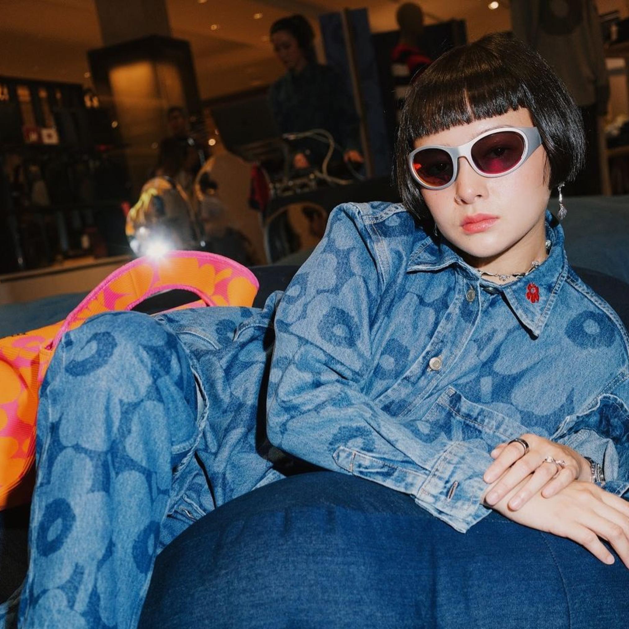 Supanaree leans against a pillow, dressed in a Unikko denim outfit and wearing sunglasses