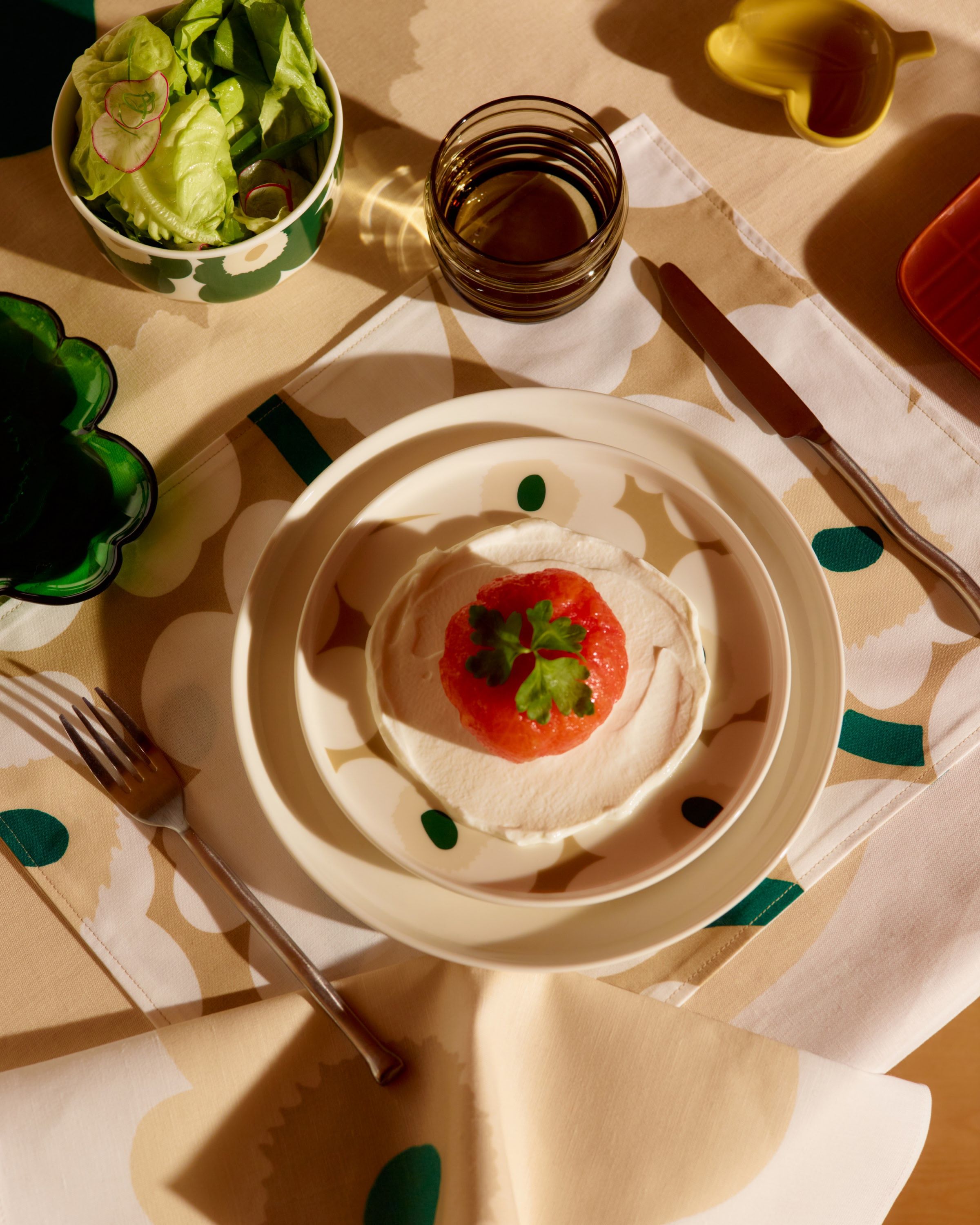 Various Marimekko tableware in Unikko print, featuring beige and green tones, arranged on a table.