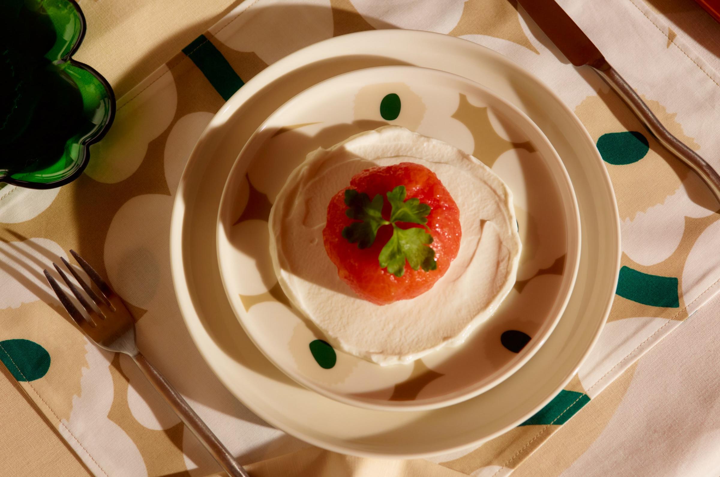 Various Marimekko tableware in Unikko print, featuring beige and green tones, arranged on a table.
