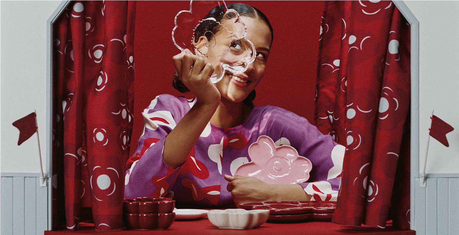 Woman holding a clear Unikko-shaped plate in front of her face at a table with Unikko dishes.