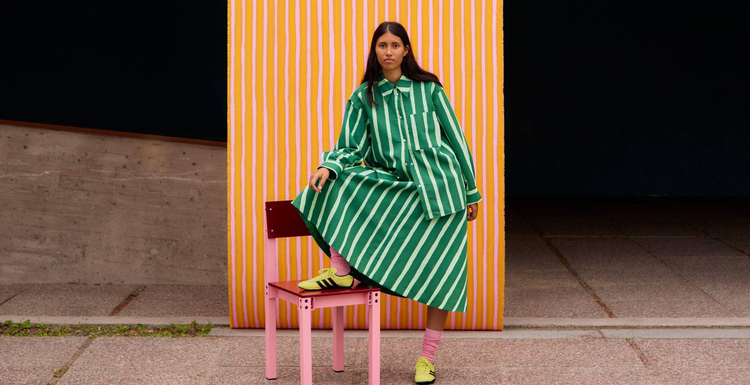 Model posing in a green stripe shirt and skit with Piccolo print in front of a concrete building and Orange Piccolo pattern fabric.