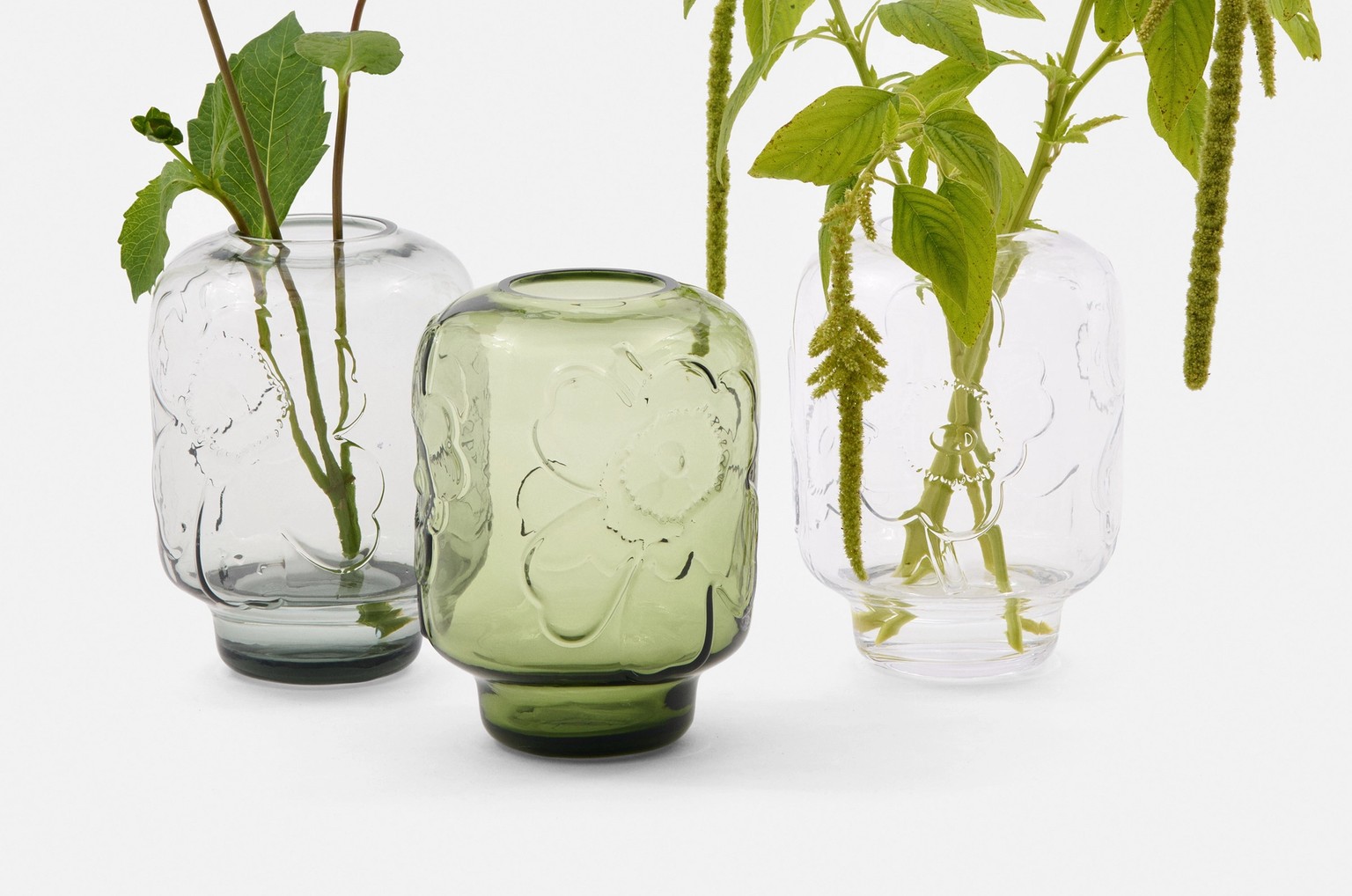 Three Unikko vases in green, grey and clear with flowers in them.