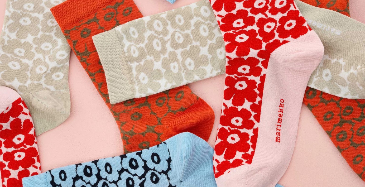 Unikko patterned socks in shades of red, beige and blue on a pink background.
