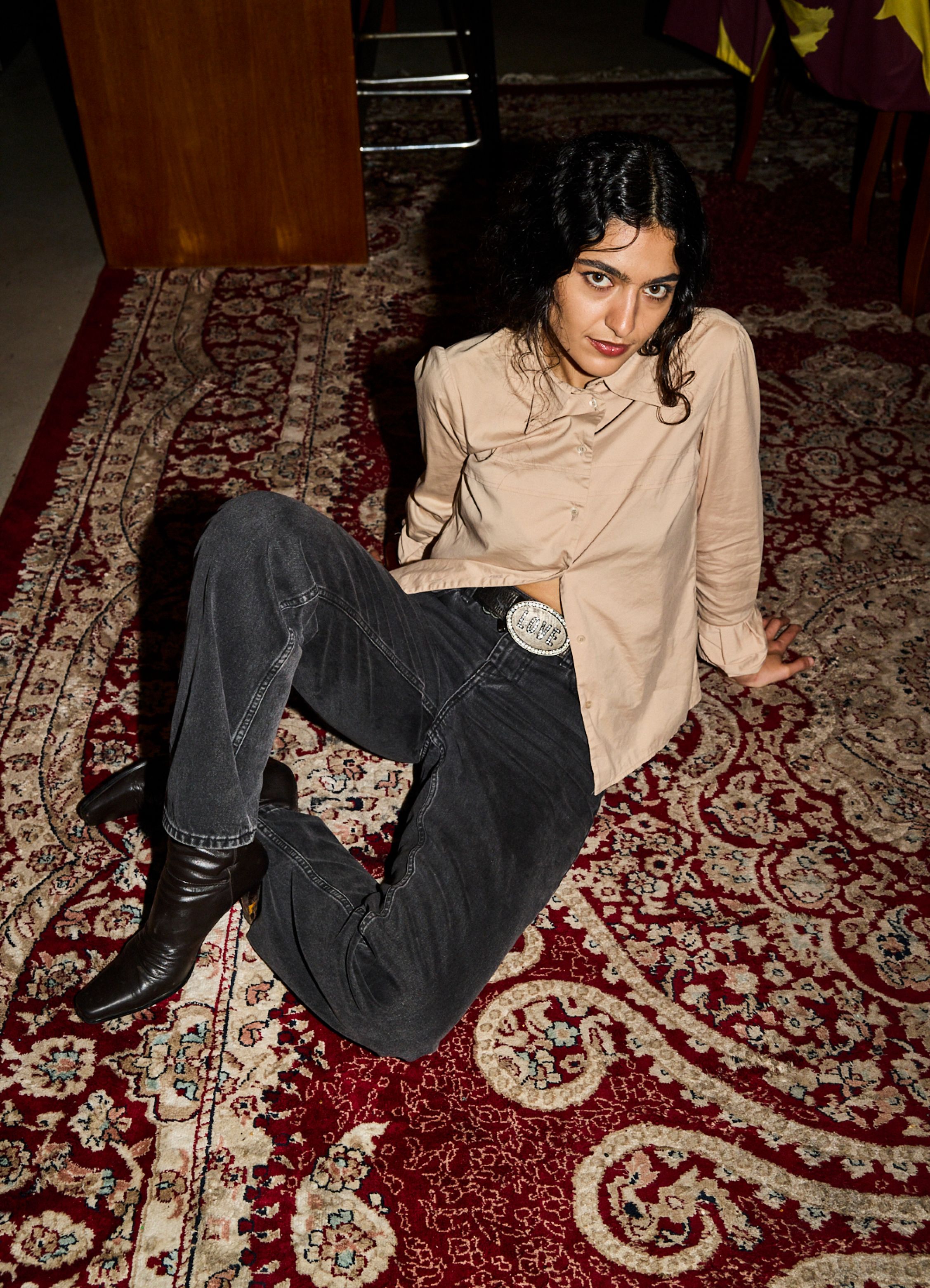 Roxie Mohebbi sits on the floor on a colorful rug, wearing black Maridenim jeans and a brown shirt