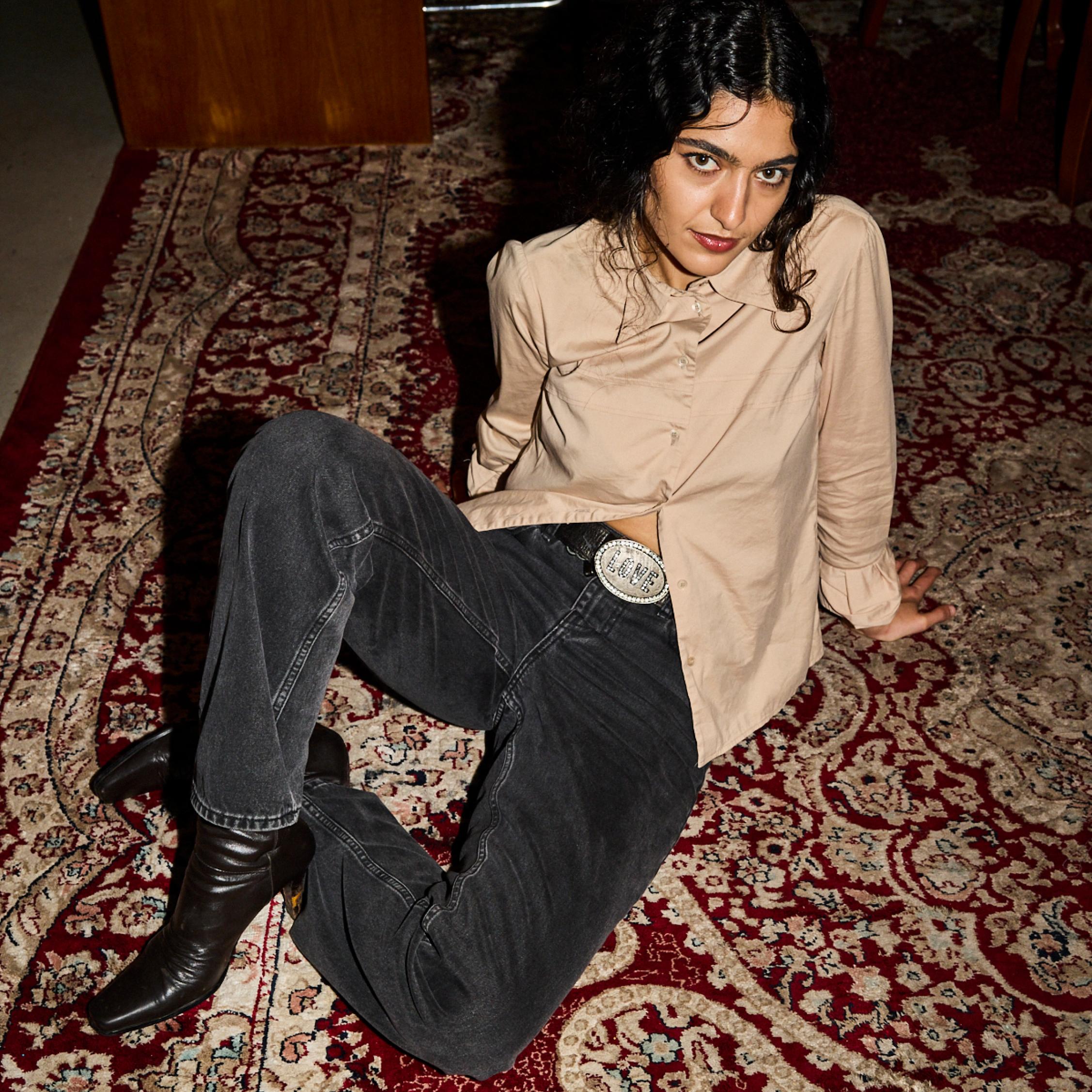 Roxie Mohebbi sits on the floor on a colorful rug, wearing black Maridenim jeans and a brown shirt