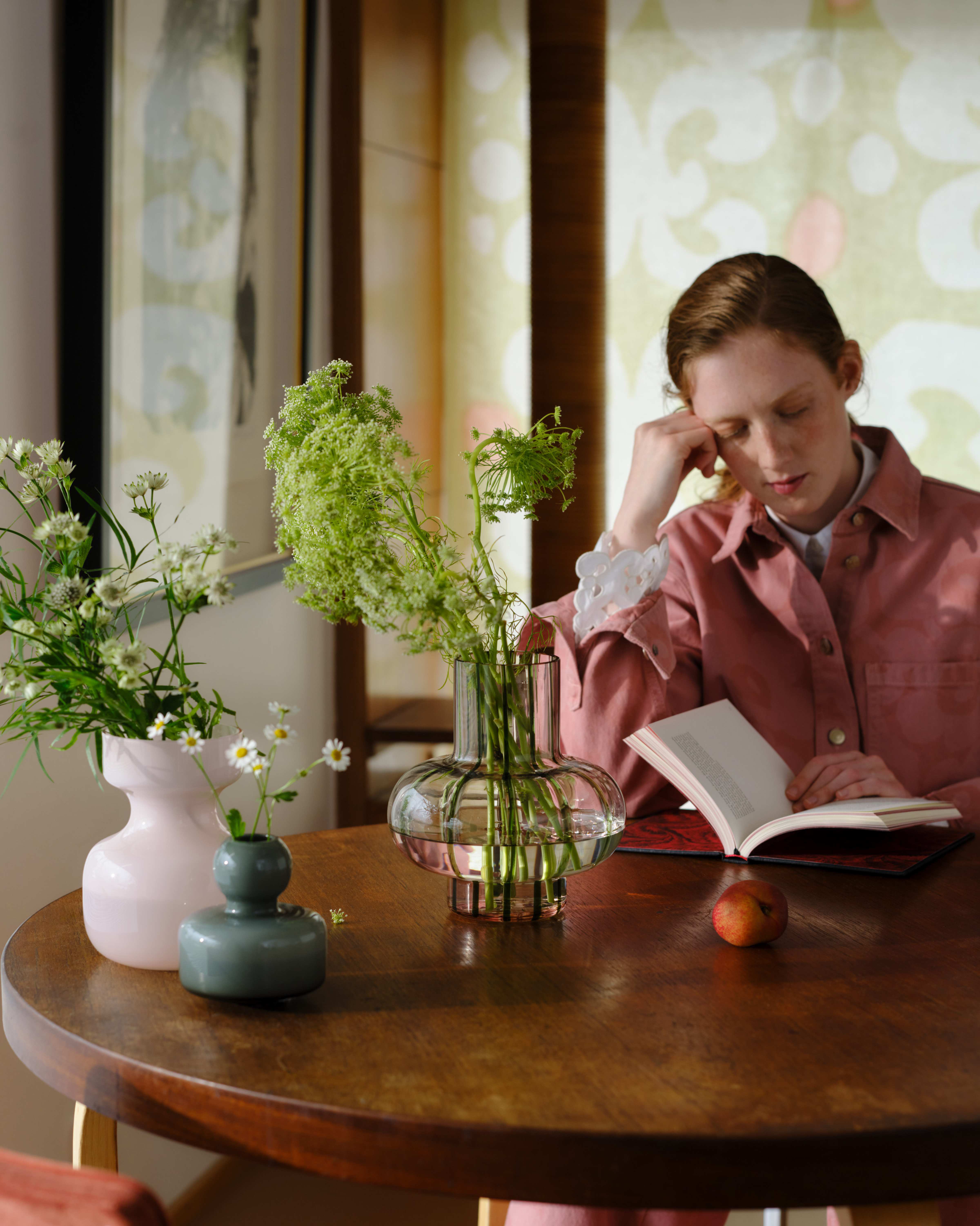 Model reading at a table with many flower-filled vases of different shapes and sizes