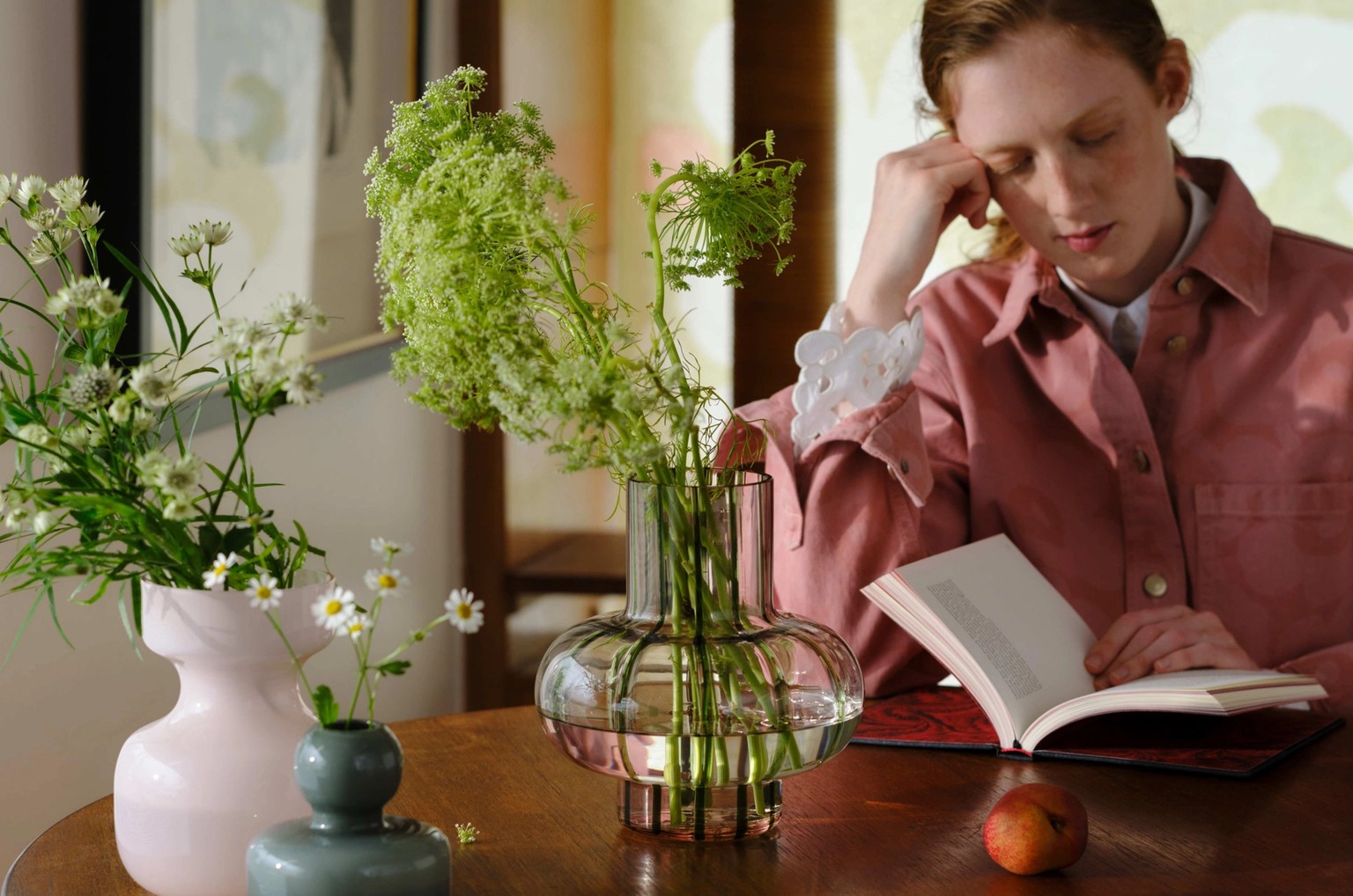 Model reading at a table with many flower-filled vases of different shapes and sizes