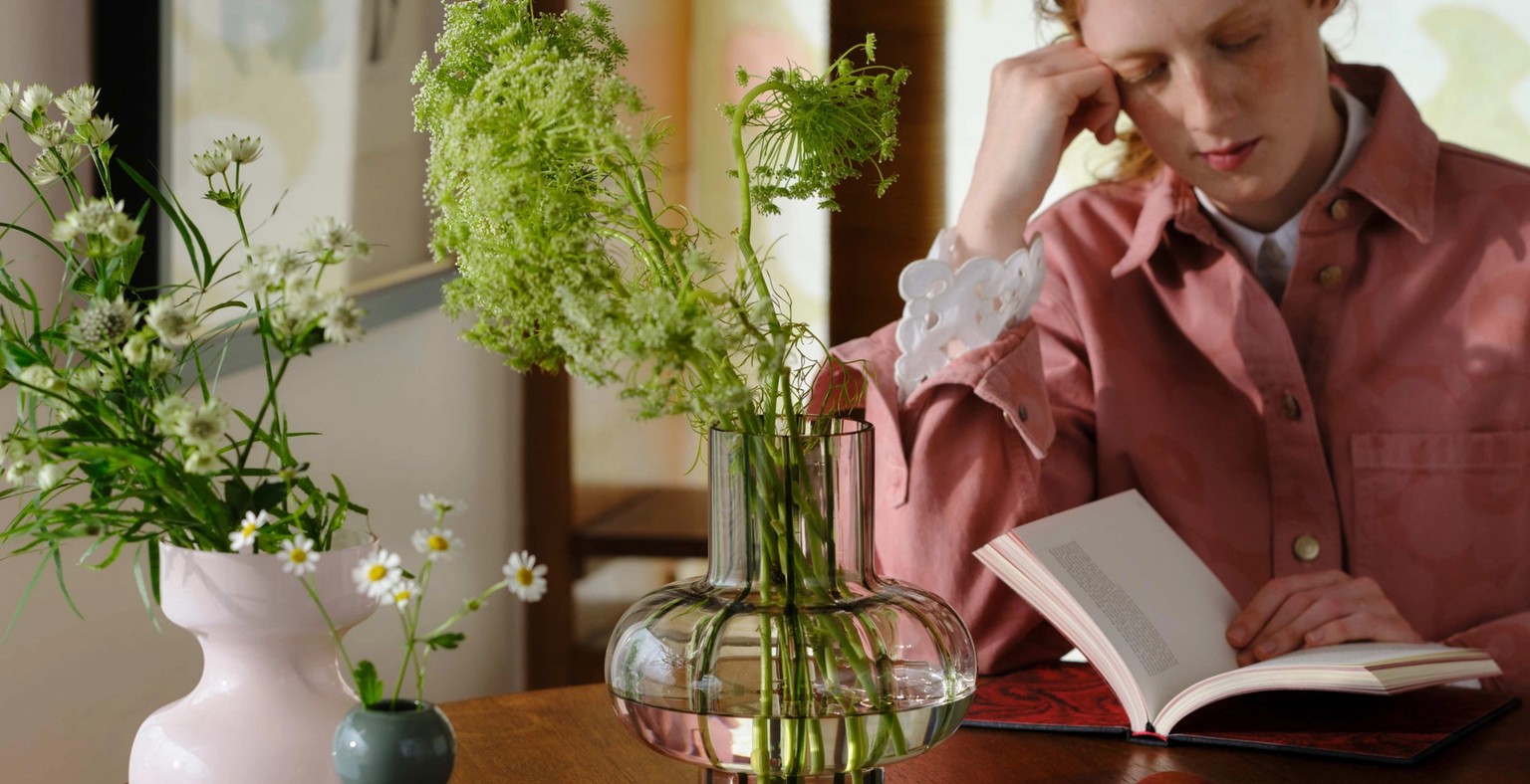 Model reading at a table with many flower-filled vases of different shapes and sizes