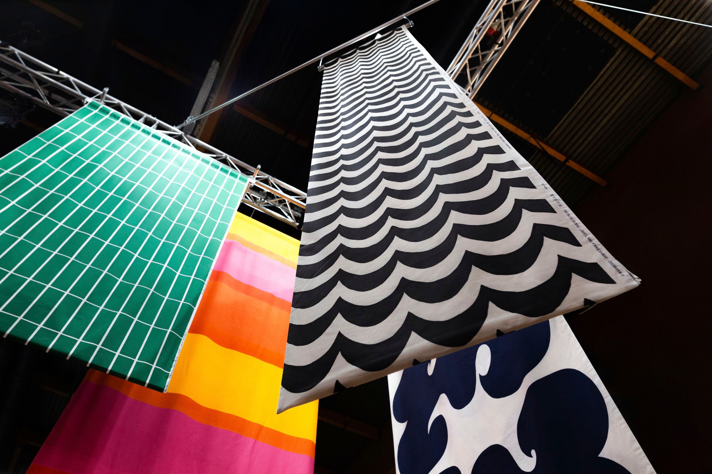 Fabrics hanging from the ceiling, with patterns: Annika Rimala's Laine and Jokeri patterns, Armi Ratia's Tiiliskivi pattern and Vuokko Eskolin-Nurmesniemi's Hennika pattern.