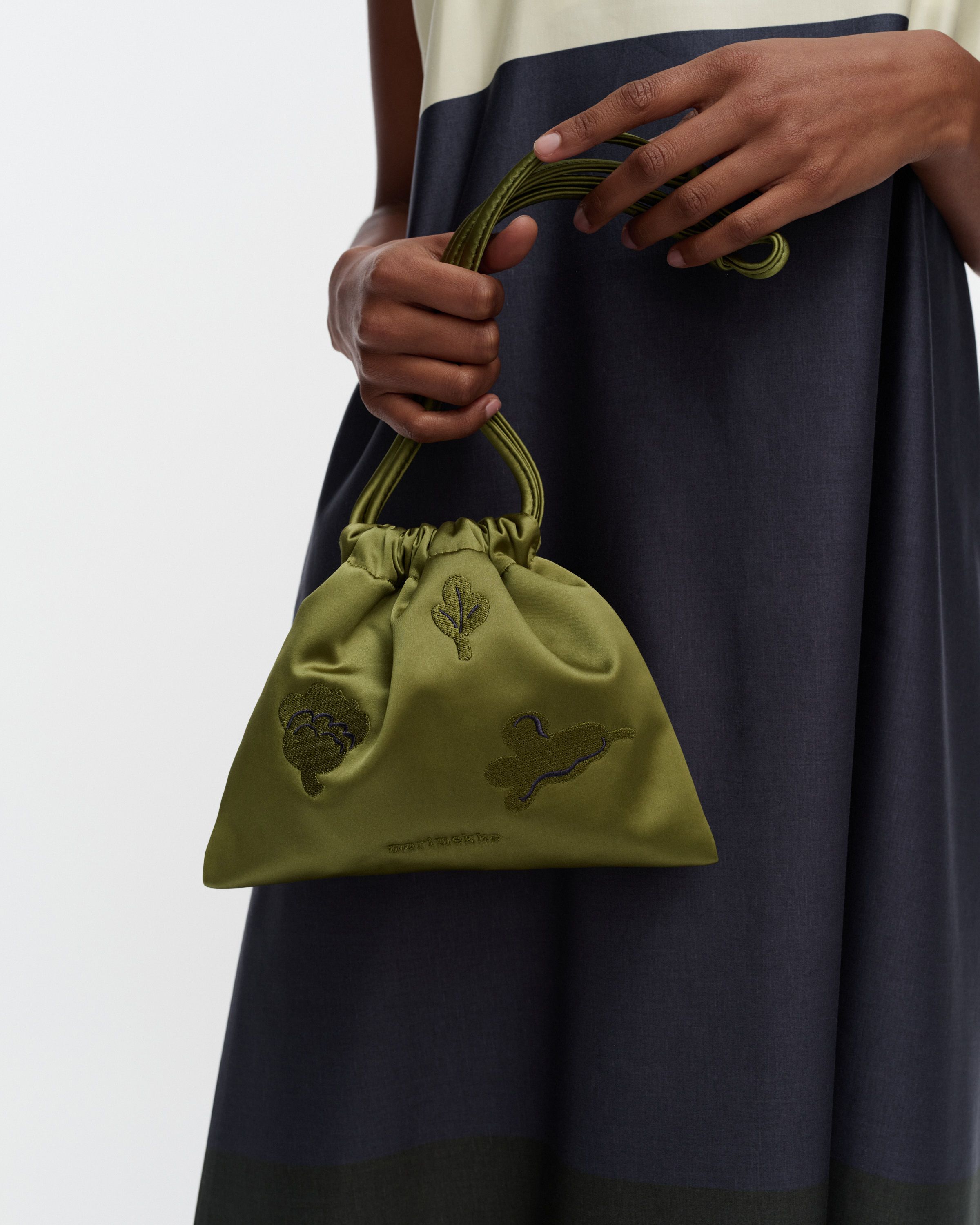 Model carrying a small green satin pouch bag in Kukasta Kukkaan print in her hands. 
