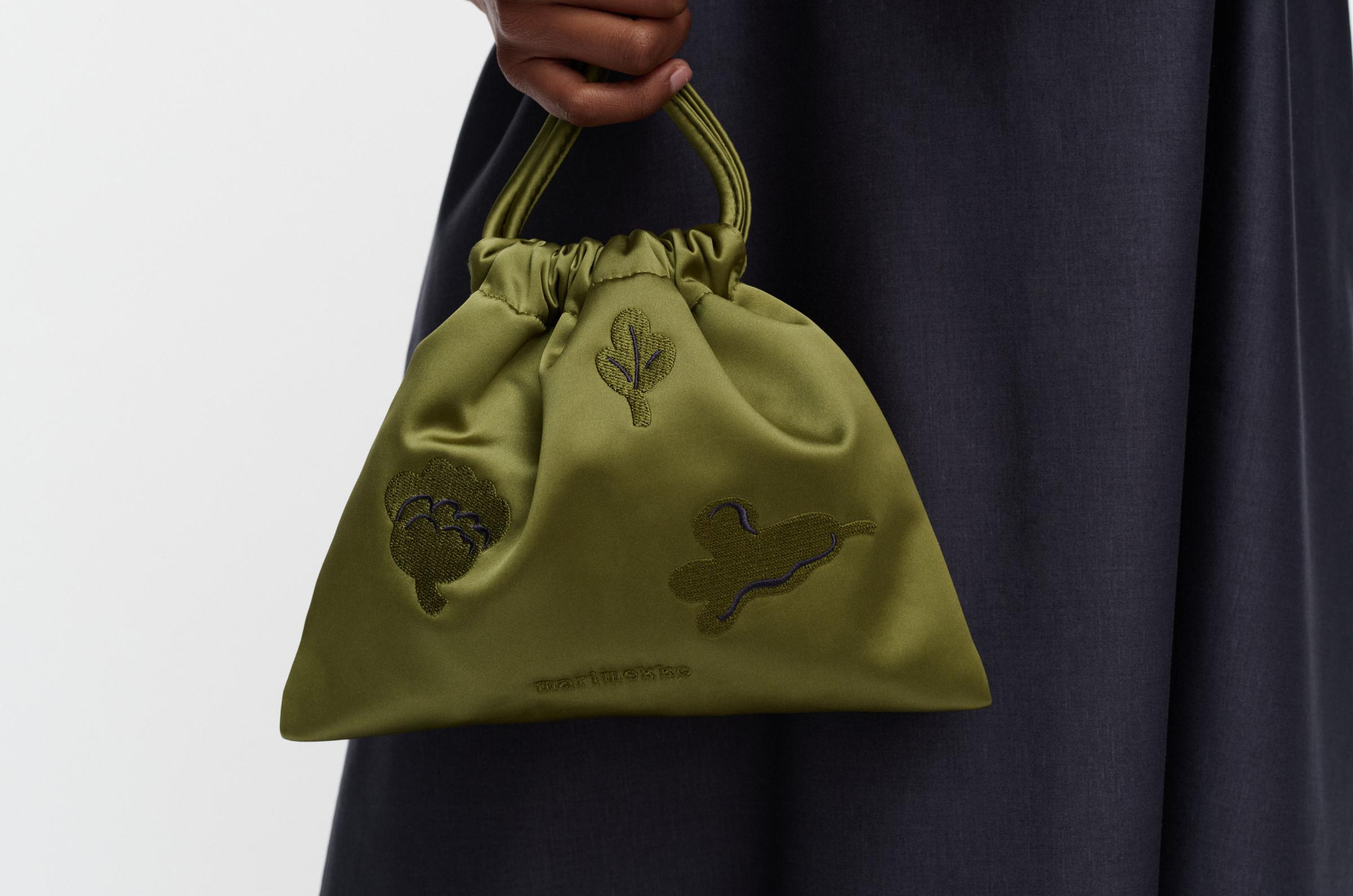 Model carrying a small green satin pouch bag in Kukasta Kukkaan print in her hands.