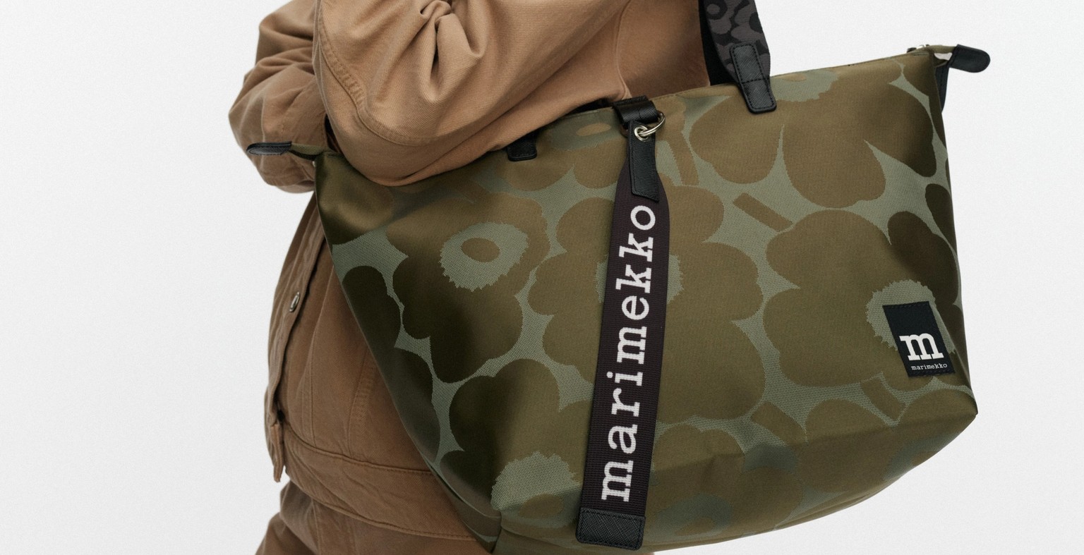 Malli kantaa vihreää keskikokoista laukkua, jossa on Unikko-painatus.