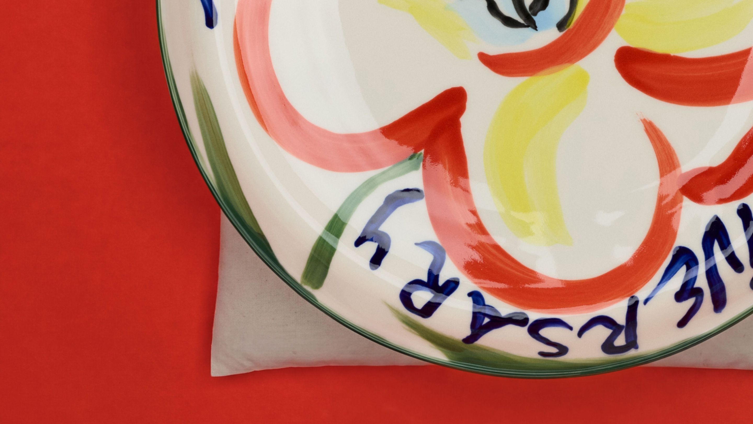 One hand-painted anniversary plate against a red background.