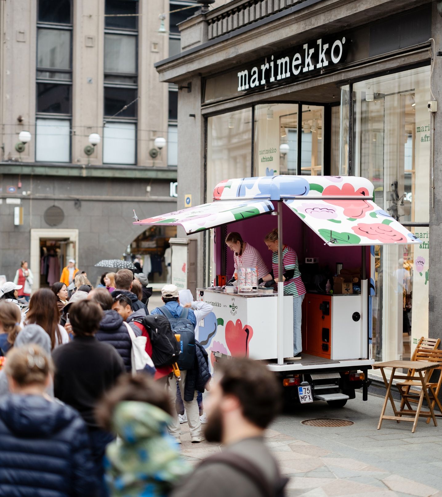 Kukasta kukkaan -kuviolla koristeltu Ape Gelato -jäätelöauto Aleksinkulman myymälän edustalla ja ihmisiä jonottamassa jäätelöä.