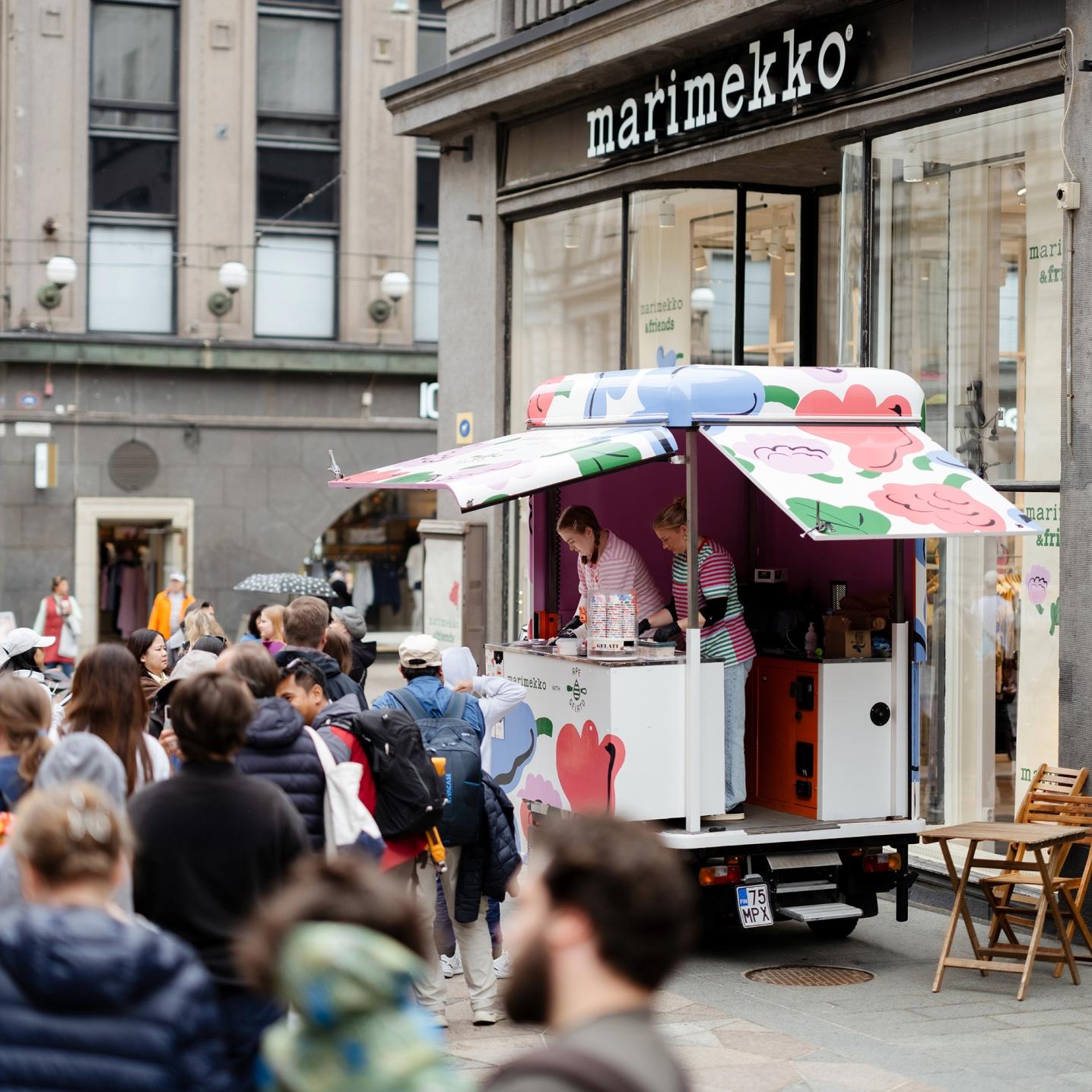 Kukasta kukkaan -kuviolla koristeltu Ape Gelato -jäätelöauto Aleksinkulman myymälän edustalla ja ihmisiä jonottamassa jäätelöä.