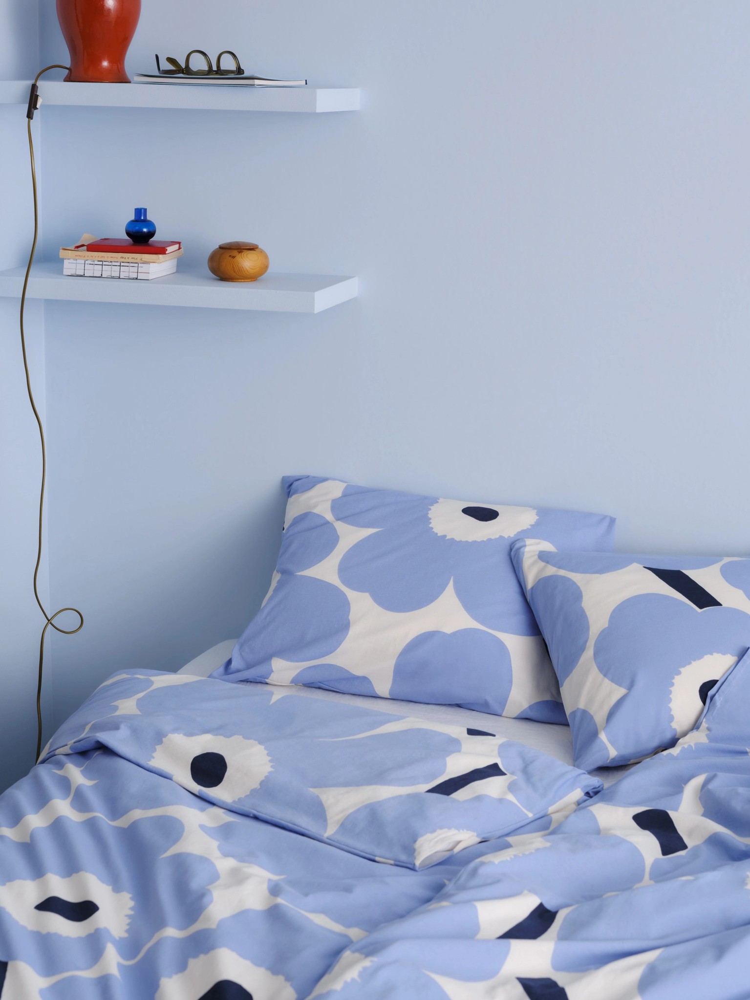 Siniset ja valkoiset Unikko-kuvioidut pussilakanat ja tyynyliinat vuoteella.