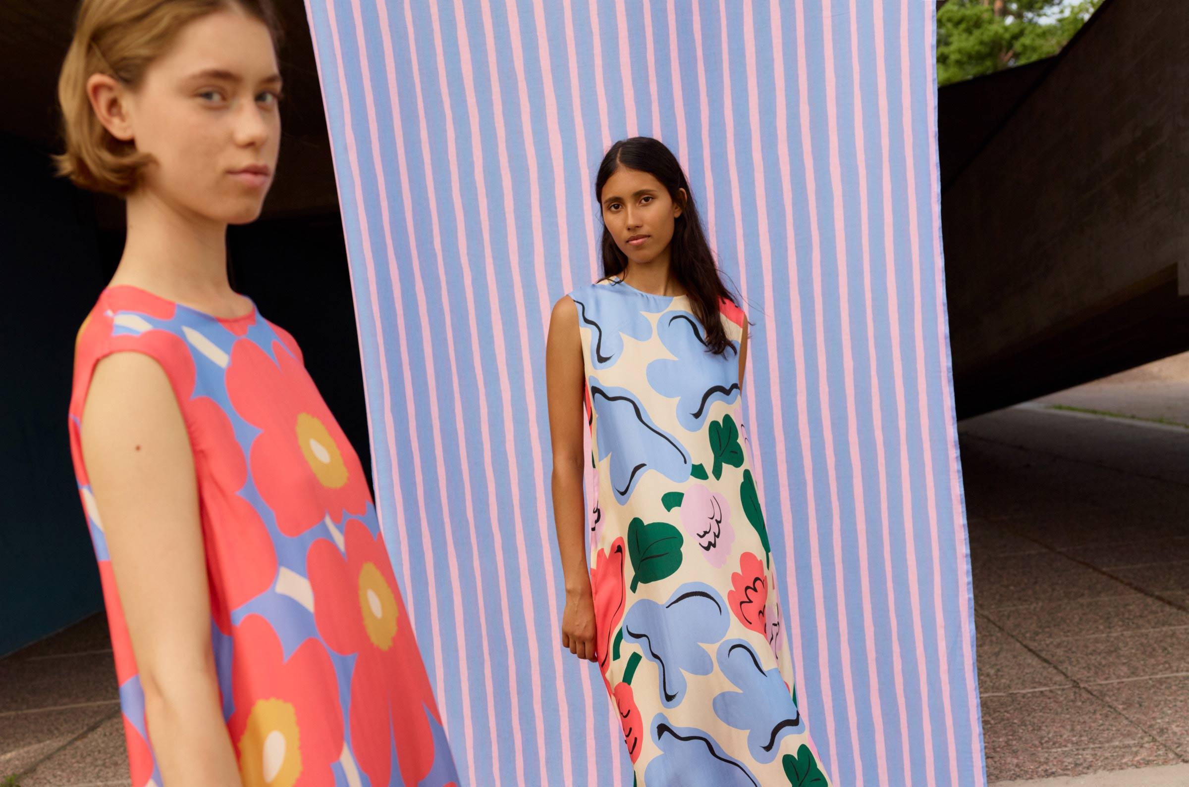 Models wearing a dress with red and blue Unikko print and a dress with blue, red, green and pink Kukasta kukkaan print.