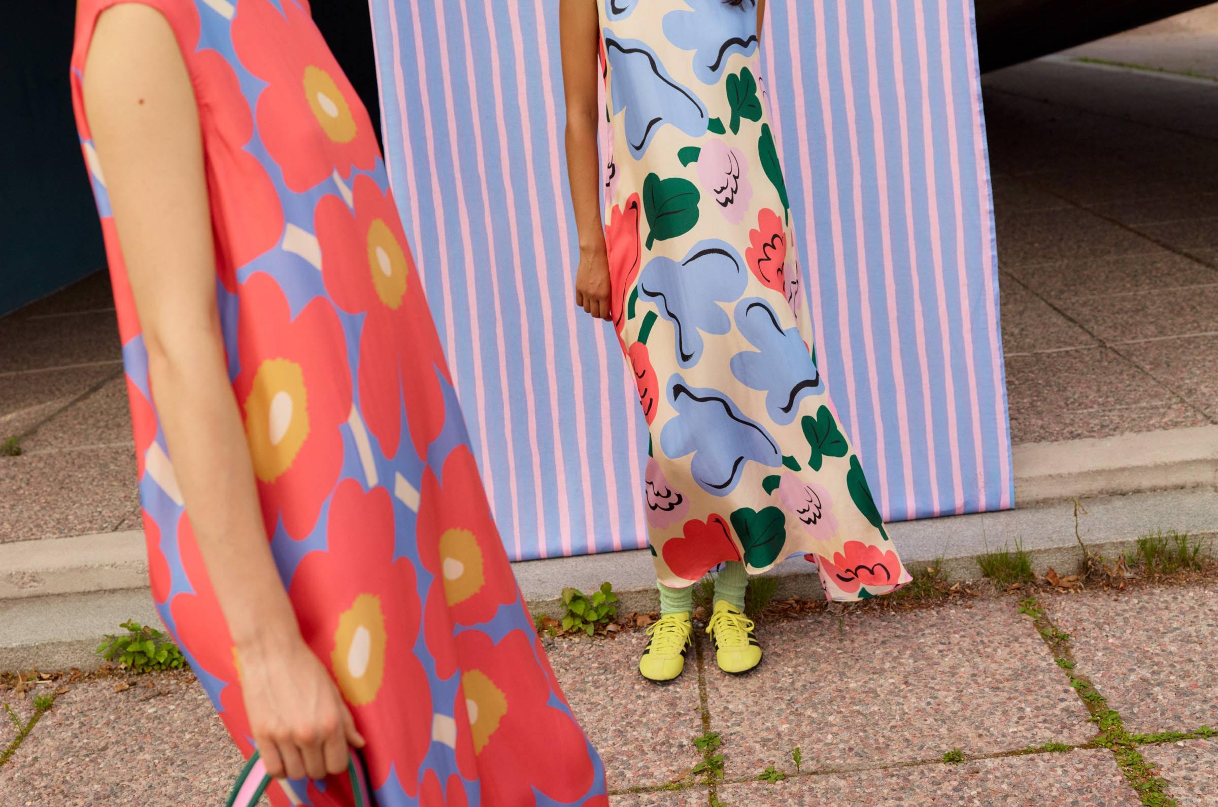 Models wearing a dress with red and blue Unikko print and a dress with blue, red, green and pink Kukasta kukkaan print.