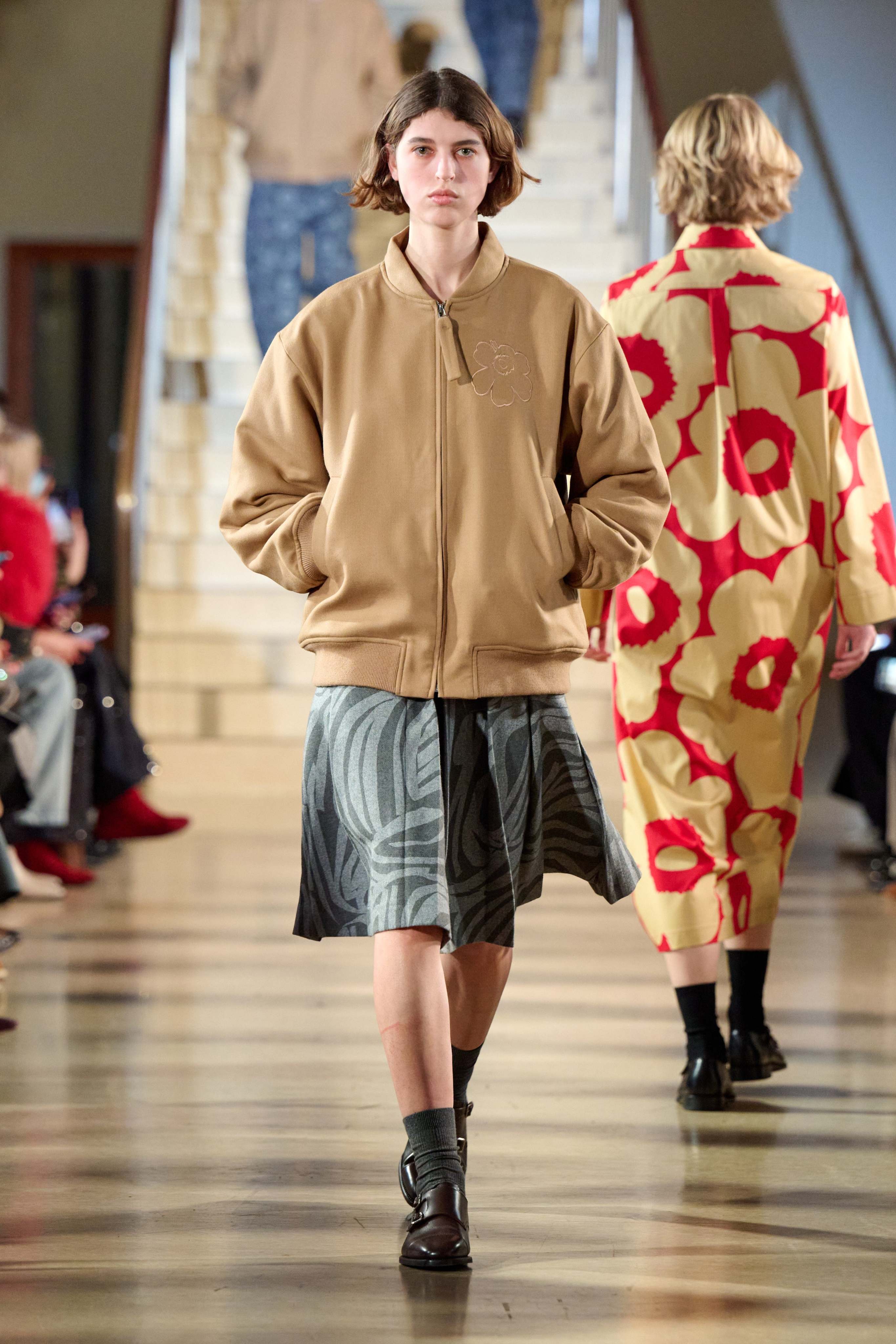 A model walking in Marimekko's fashion show wearing brown Unikko-coat and grey skirt