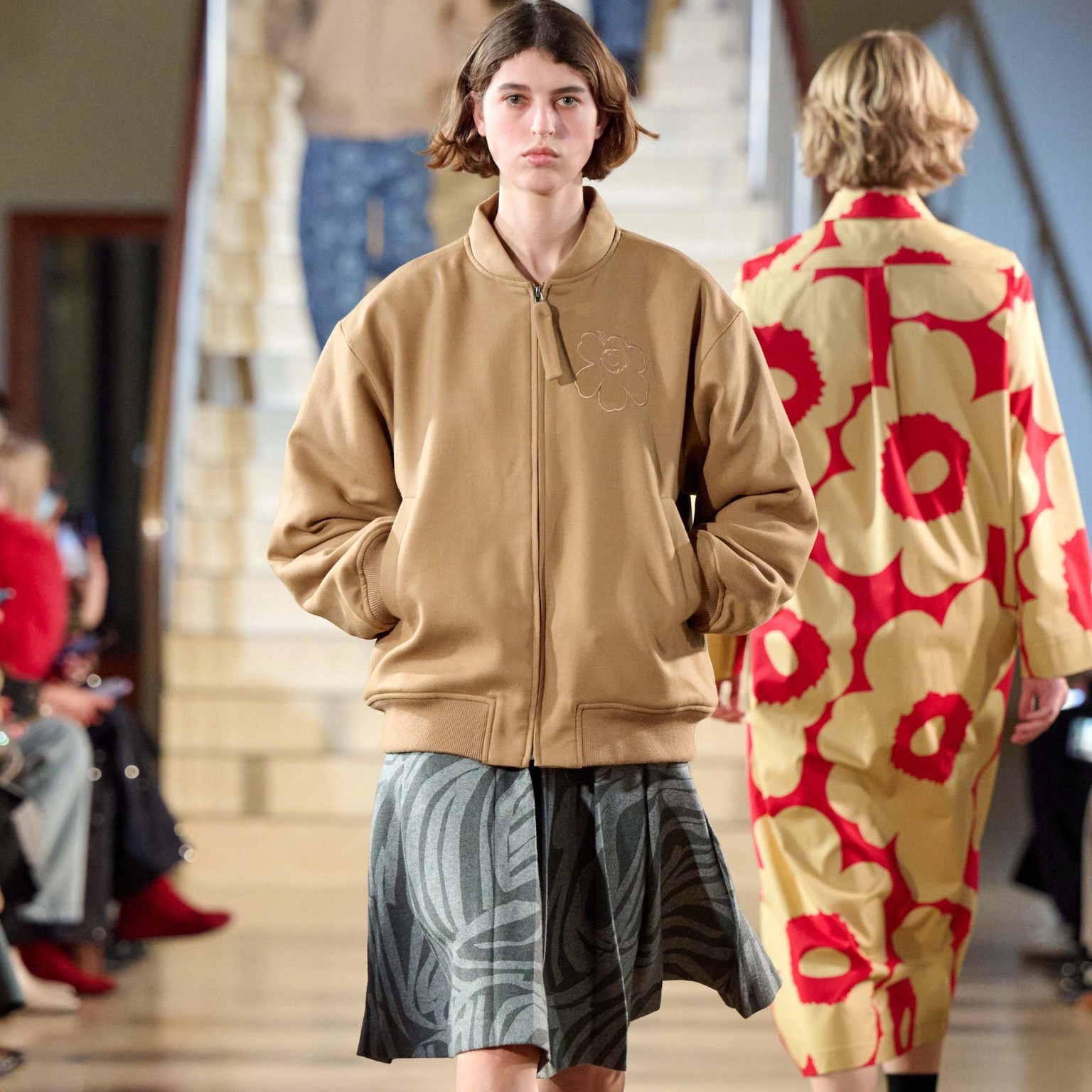 A model walking in Marimekko's fashion show wearing brown Unikko-coat and grey skirt