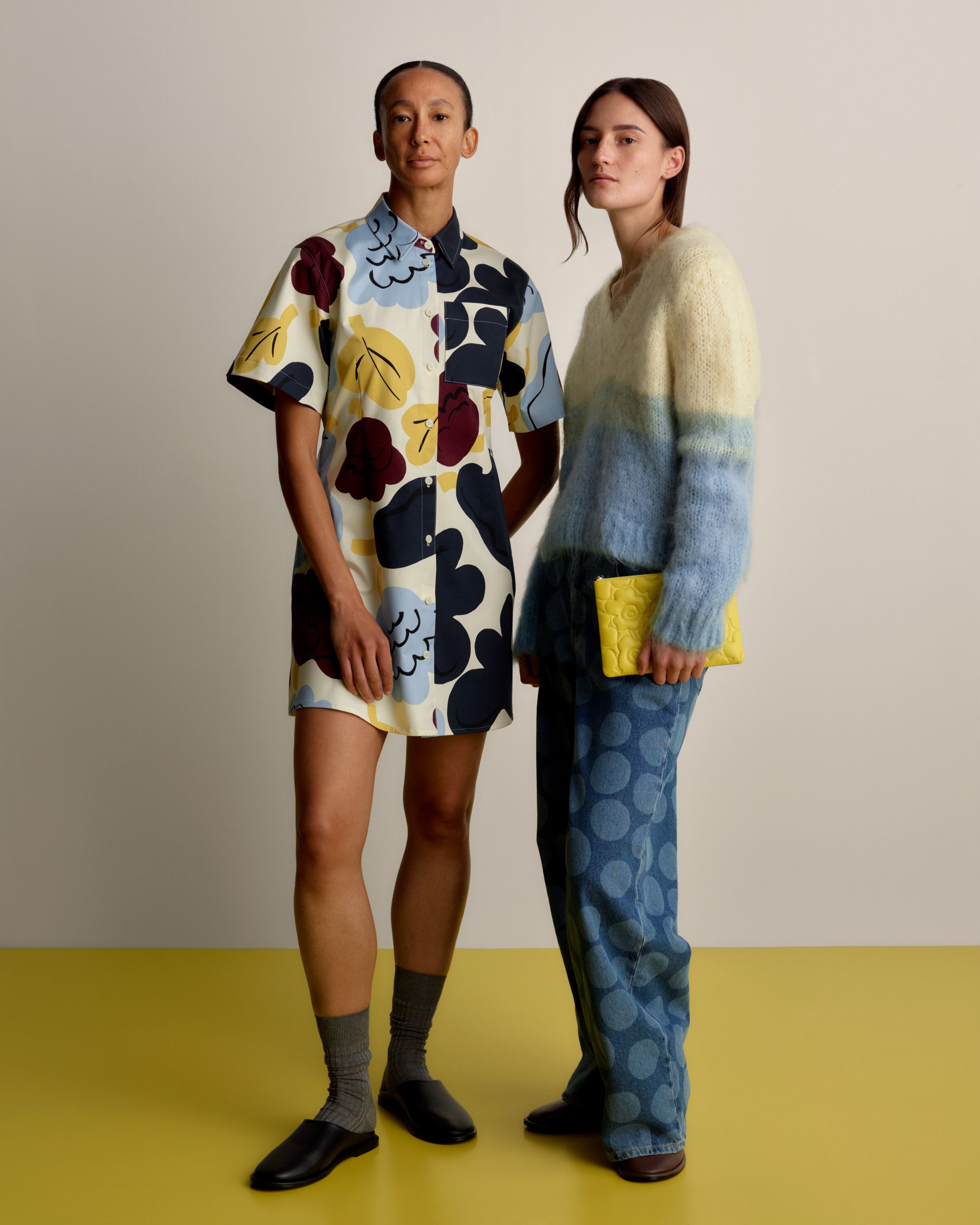 Two models, one wearing a Seikkailu dress in the Kukasta Kukkaan print and the other a Utuinen sweater and Maridenim Loose jeans in the Petrooli print.