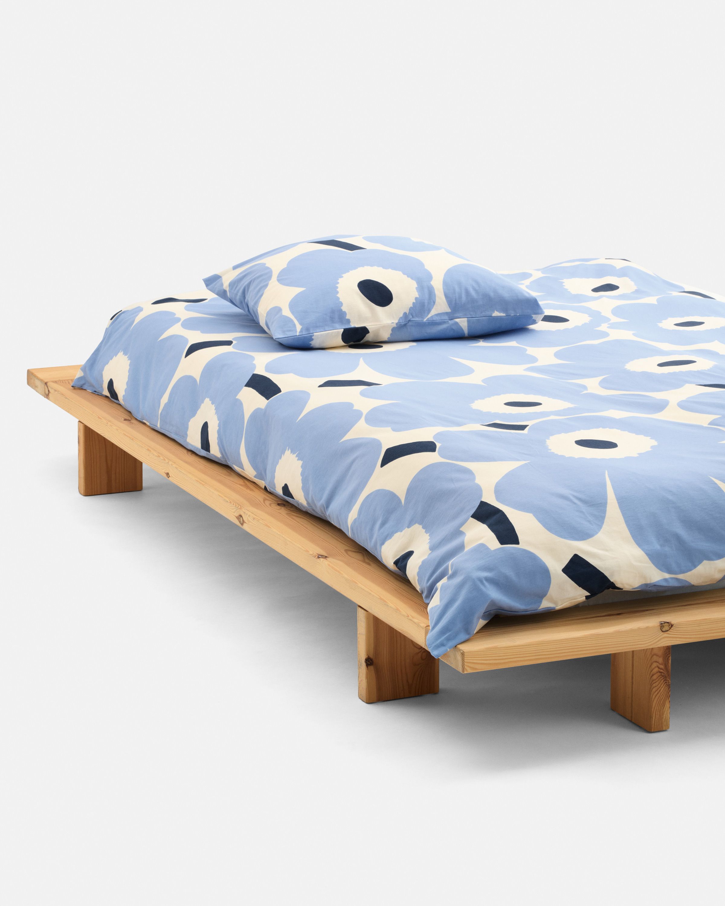 A made bed with light blue Unikko pattern sheets.