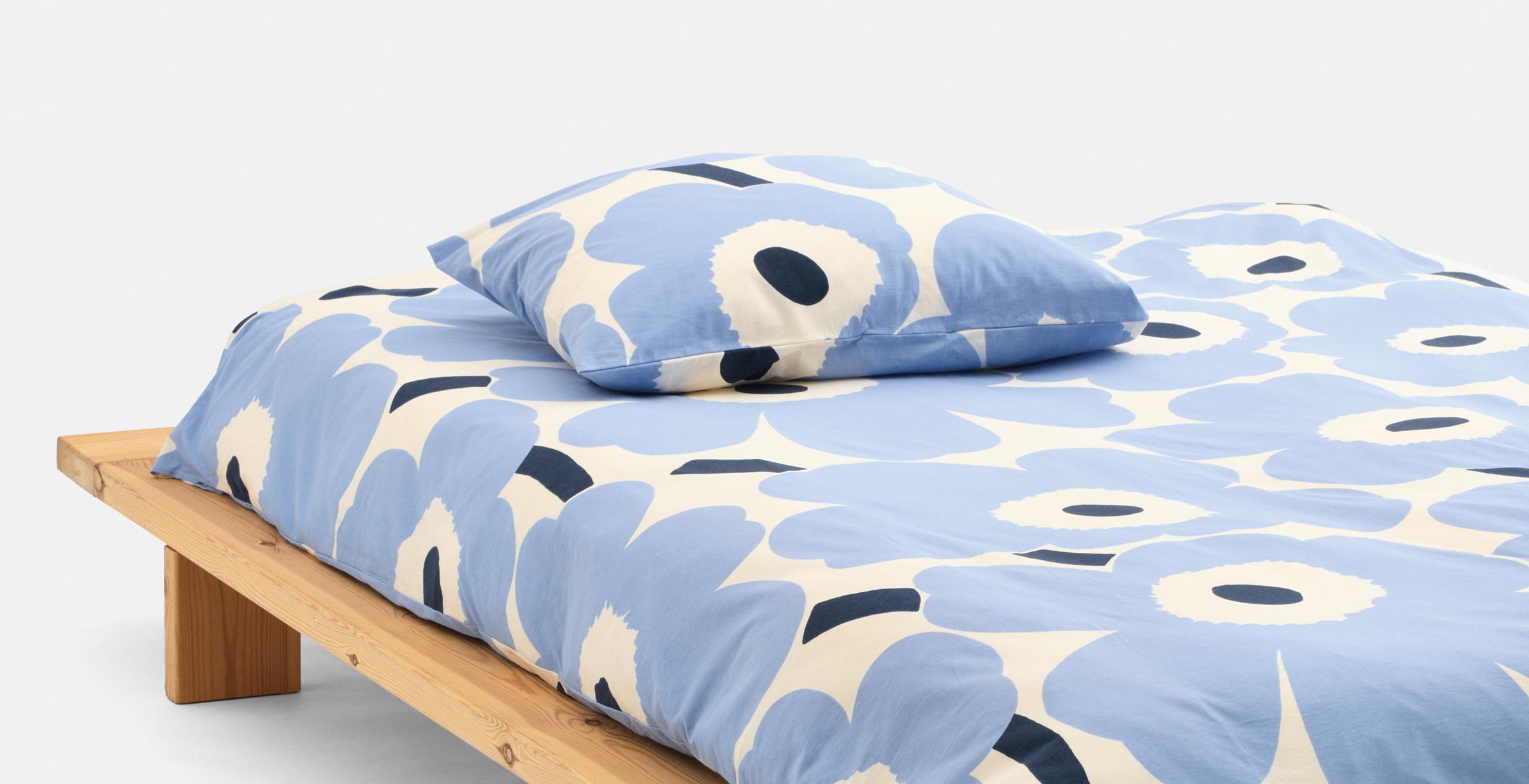 A made bed with light blue Unikko pattern sheets.