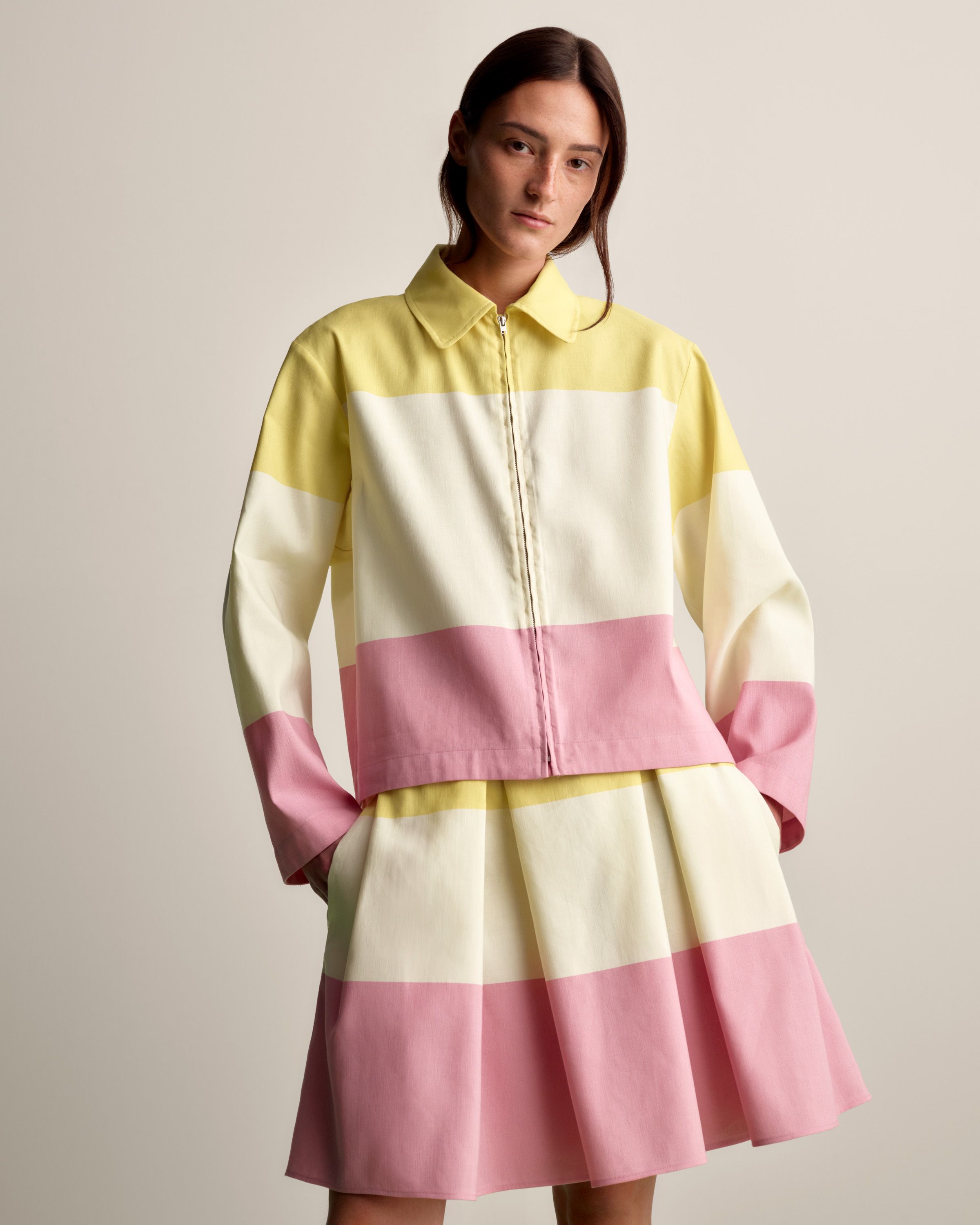 Model wearing a collar shirt with zipper in front and skirt in matching pink and yellow Hennika print. 