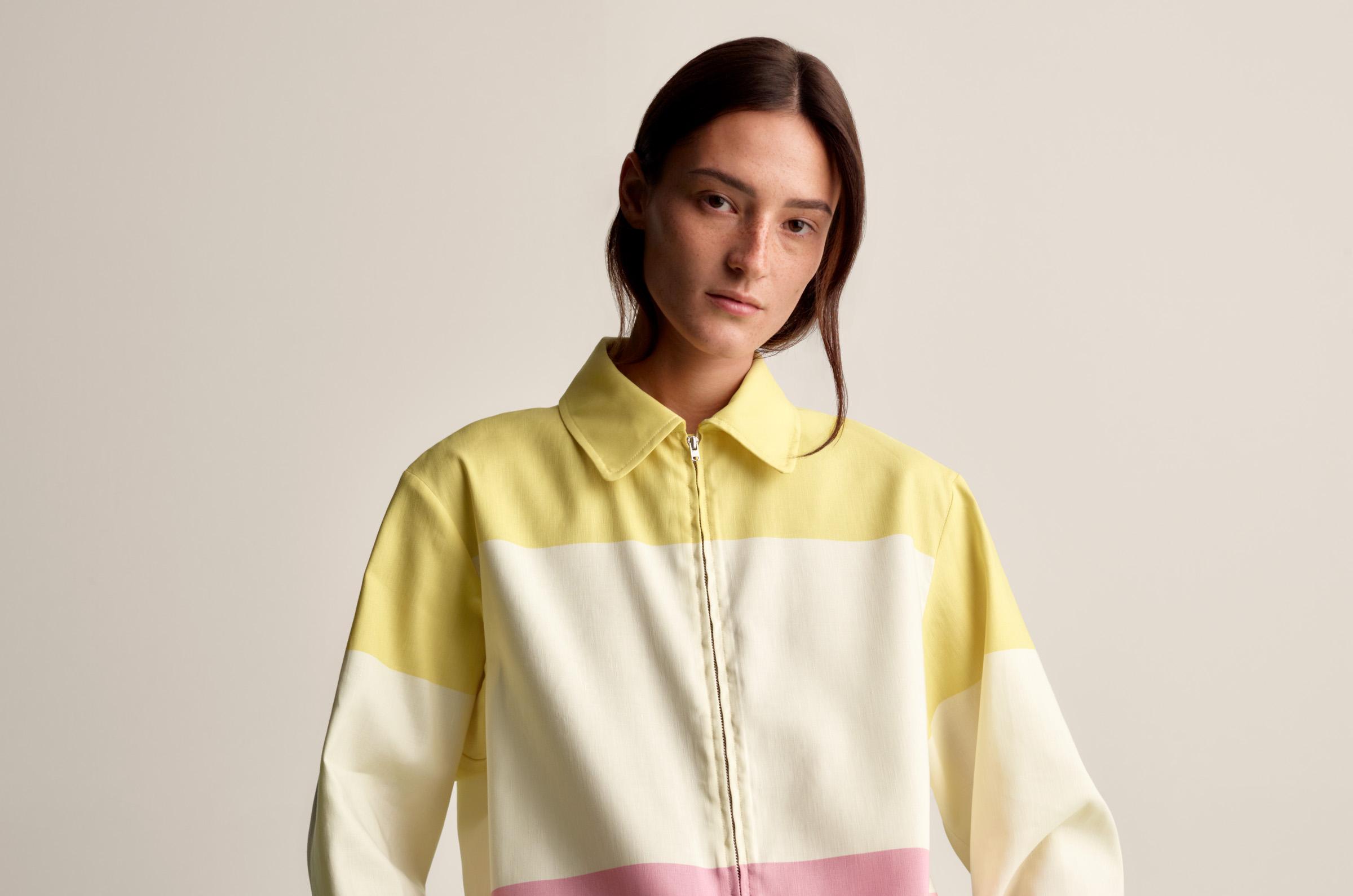 Model wearing a collar shirt with zipper in front and skirt in matching pink and yellow Hennika print.