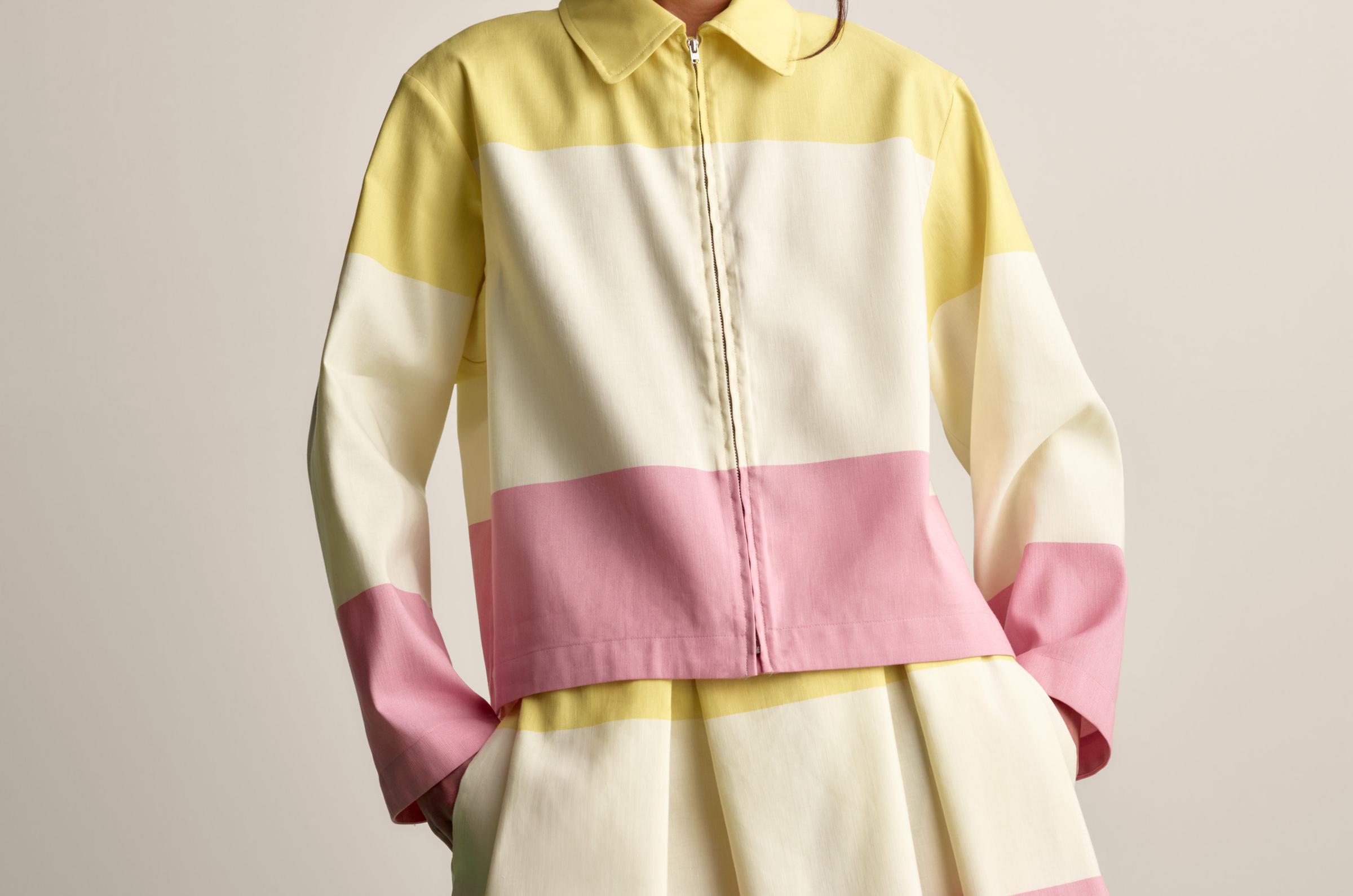 Model wearing a collar shirt with zipper in front and skirt in matching pink and yellow Hennika print.