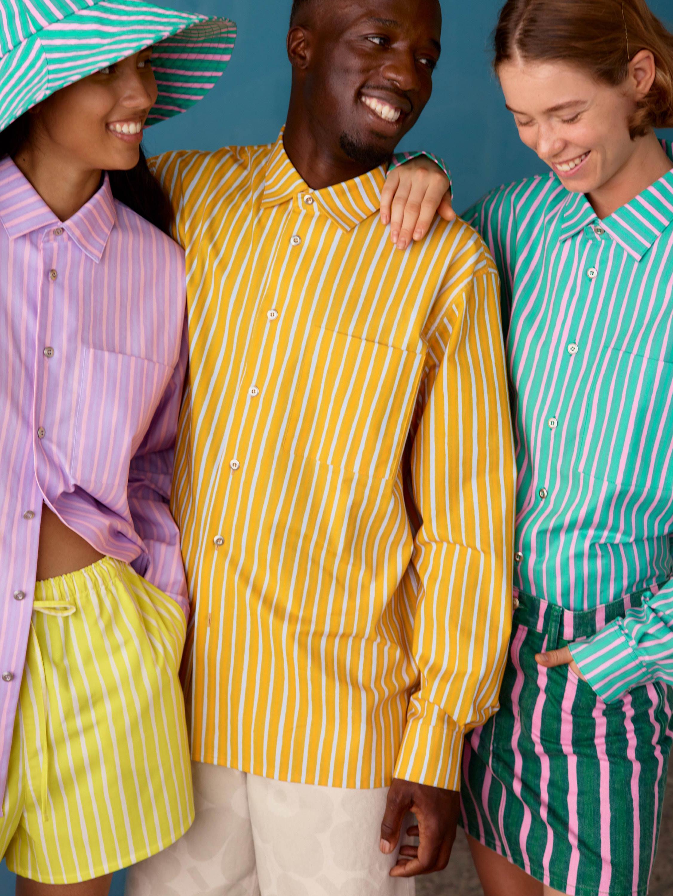 Three models wearing Jokapoika shirts in pink, yellow and blue Piccolo prints.