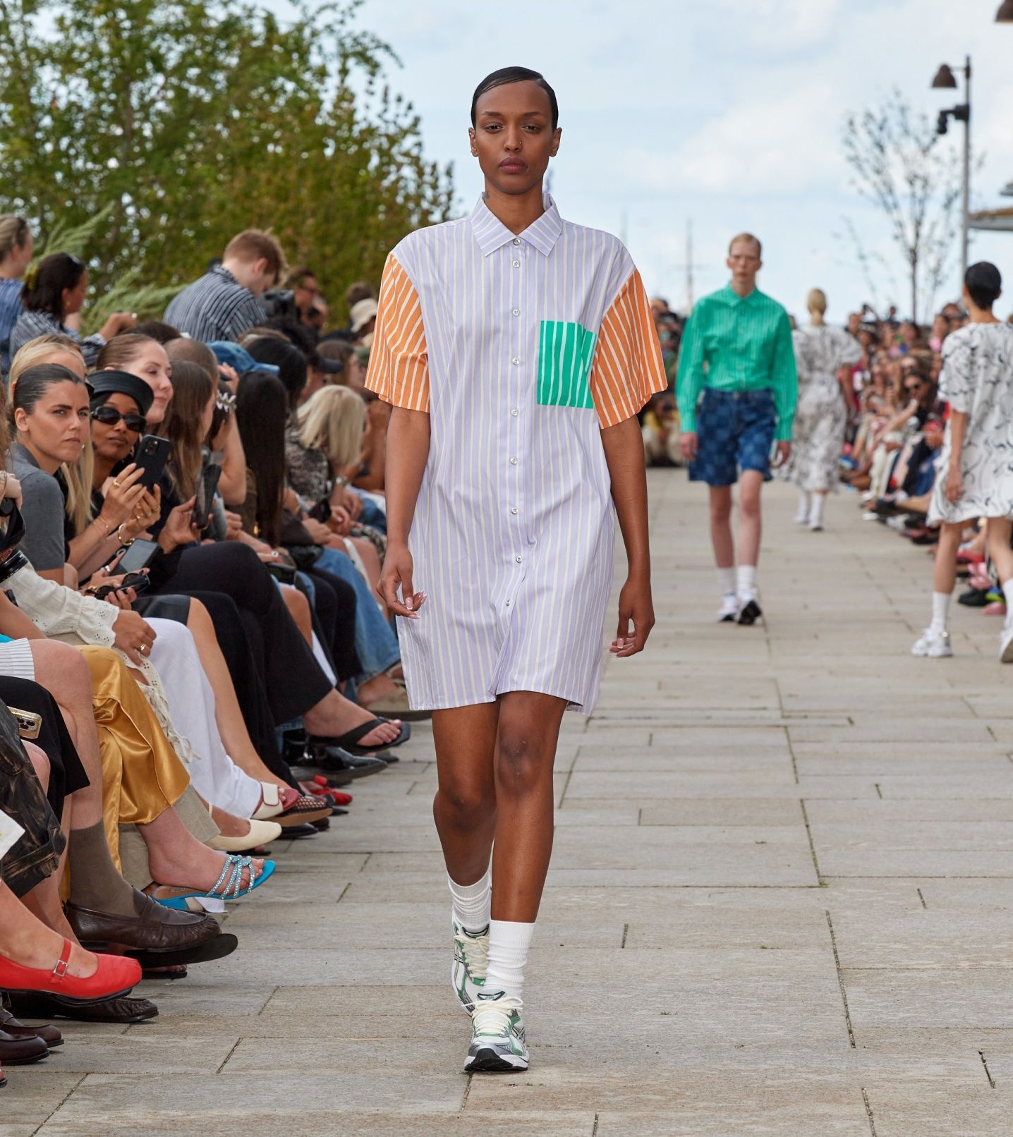 A model walking on the catwalk of a fashion show dressed in a colorful Jokapoika dress with t-shirt sleeves.