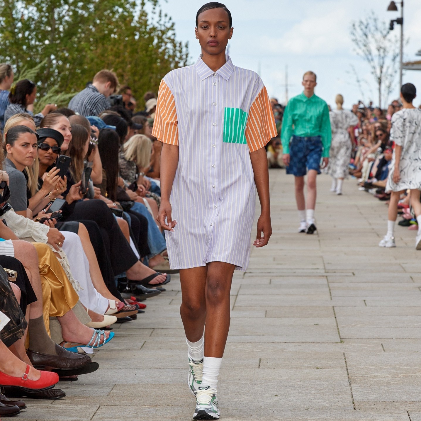 A model walking on the catwalk of a fashion show dressed in a colorful Jokapoika dress with t-shirt sleeves.