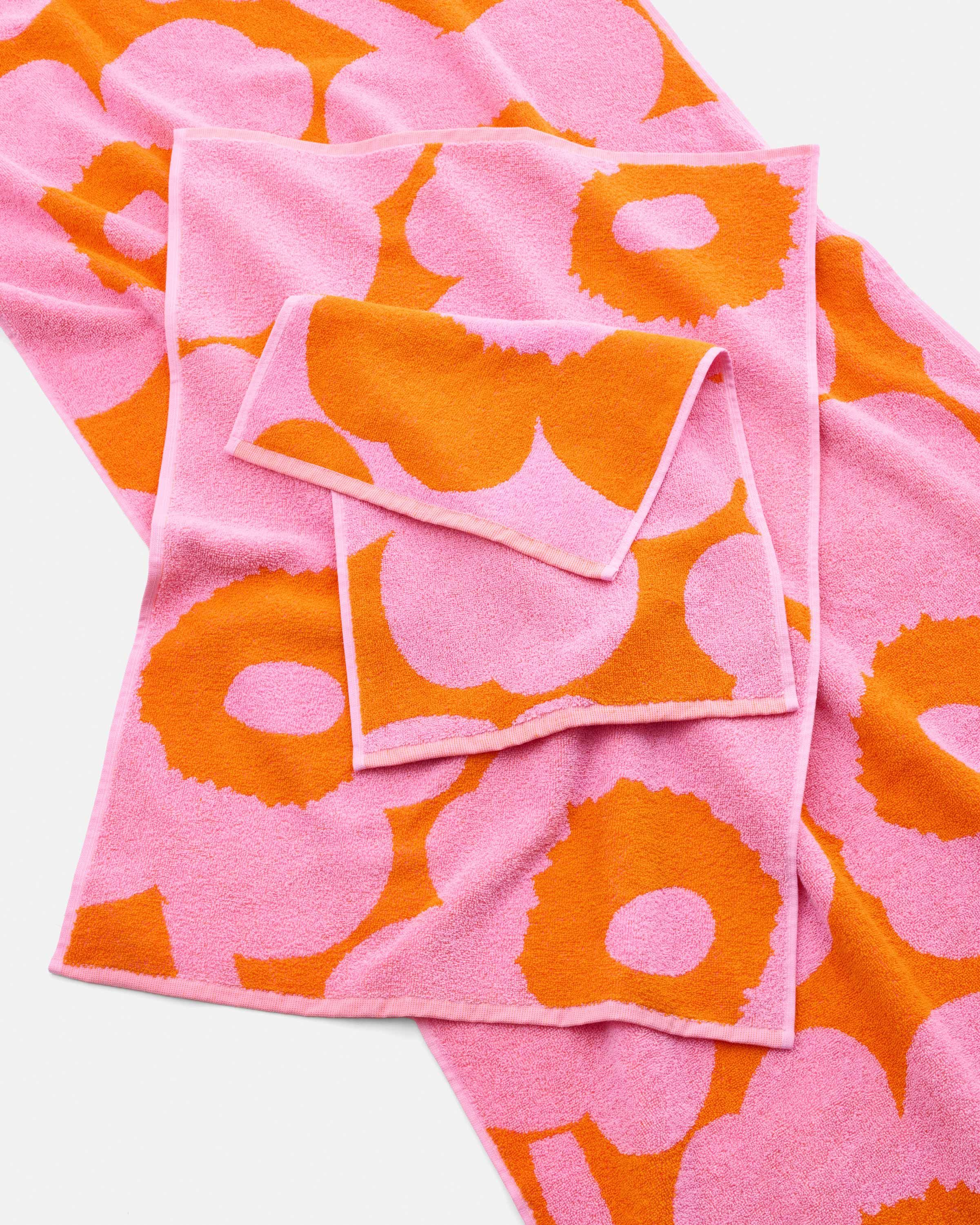 Different sized pink and orange Unikko towels spread on a flat surface.