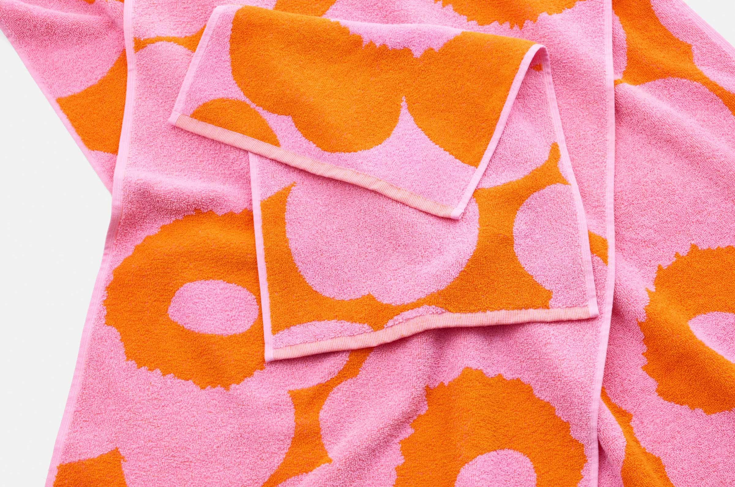 Different sized pink and orange Unikko towels spread on a flat surface.