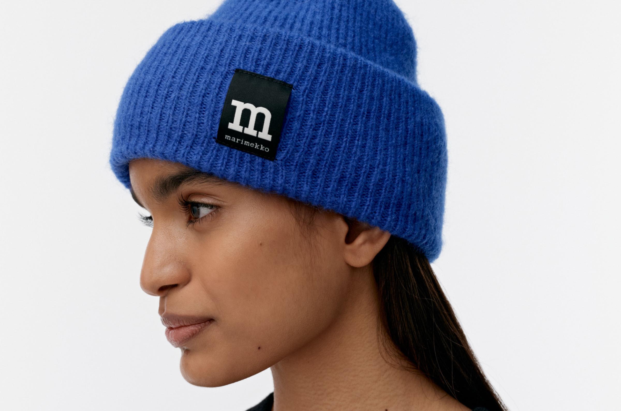 Model wearing blue beanie and black and grey Unikko knit