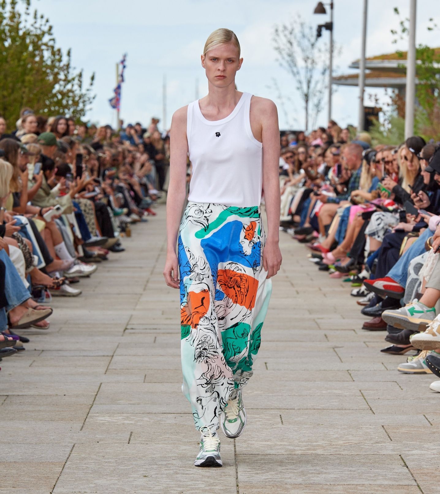 Model walking on the catwalk of the fashion show dressed in a white top and a Keveä Blomblom skirt.