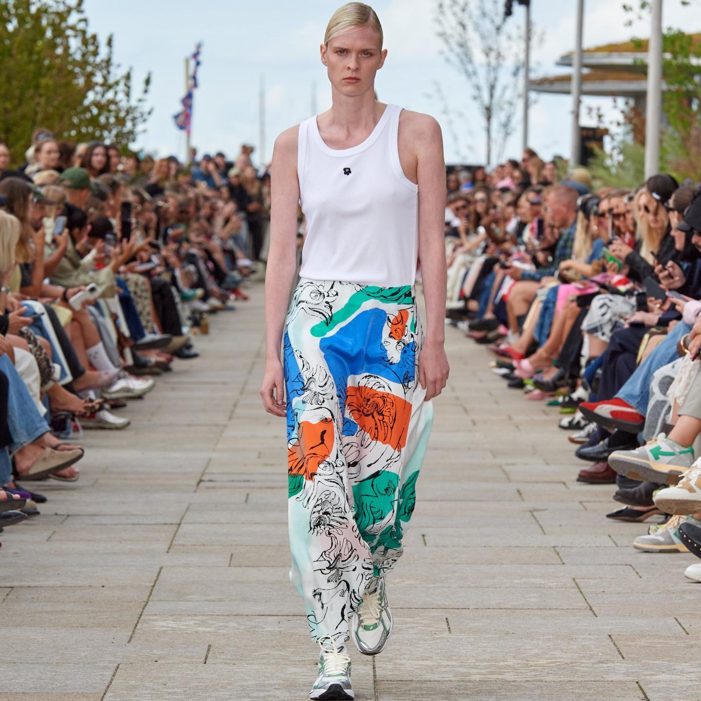Model walking on the catwalk of the fashion show dressed in a white top and a Keveä Blomblom skirt.