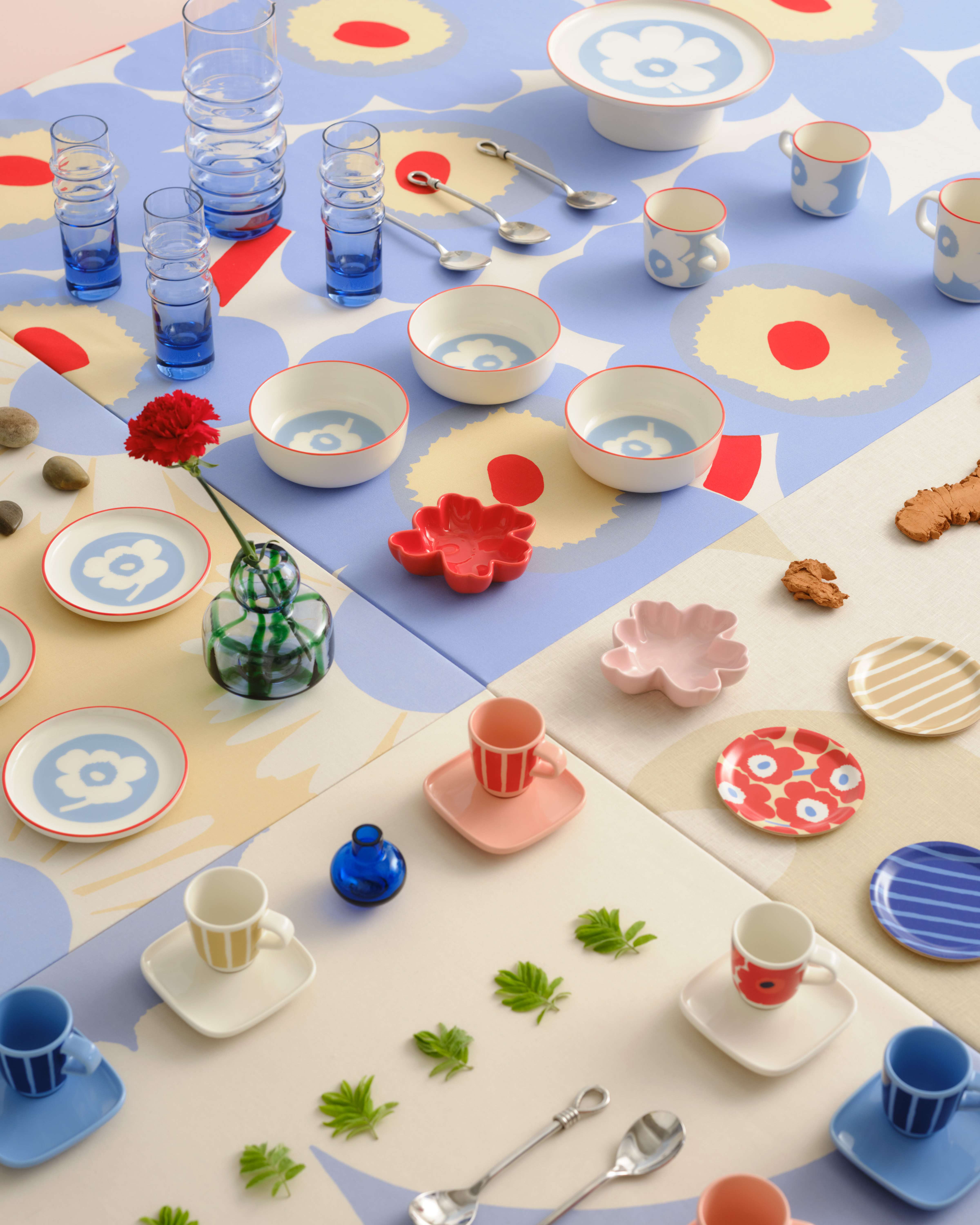 Various Marimekko glassware and tableware in Unikko and Piccolo prints, including plates, bowls, mugs, espresso cups, and coasters, arranged in rows on a large table