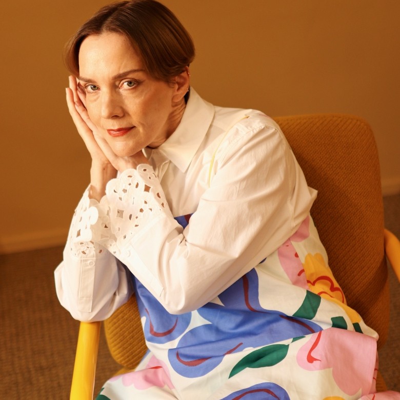 Nainen (Maria Veitola), jolla on päällään mekko Kukasta kukkaan-kuosissa ja kauluspaita Keidas-kuvioinnilla. Vasemmassa alakulmassa on pystysuora teksti "Marimekko".